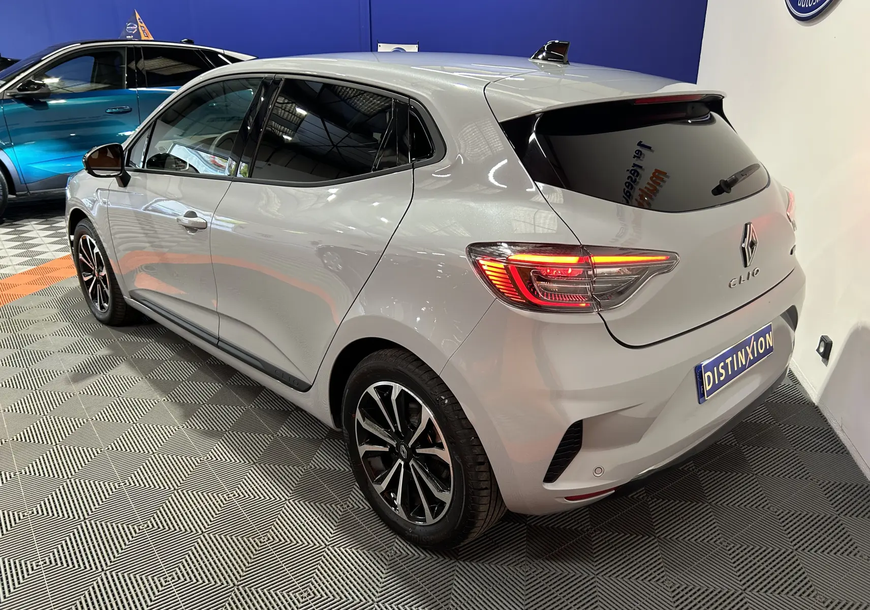 Vue 3/4 arrière droite d'une Renault Clio V gris Rafale avec feux allumés dans un showroom.