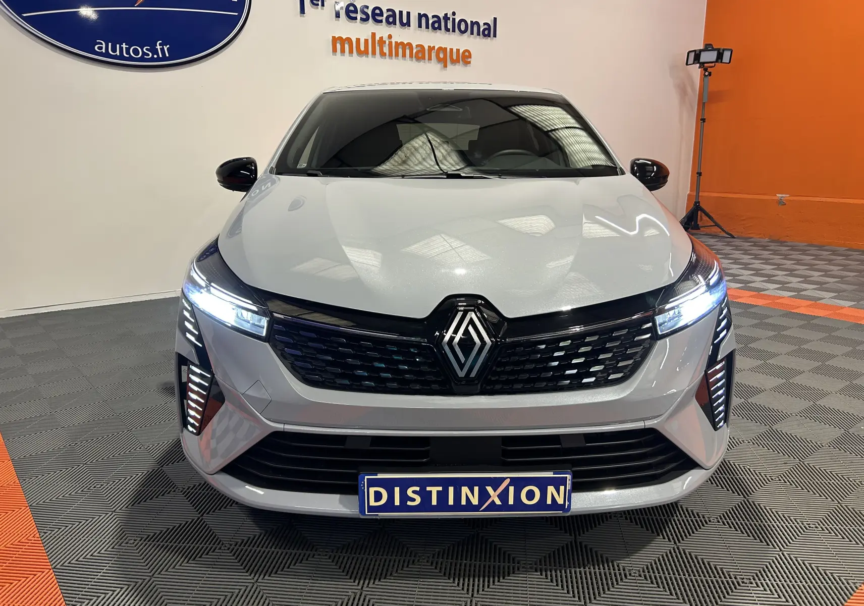 Vue frontale d'une Renault Clio V E-Tech Full Hybrid 145 gris Rafale avec phares LED allumés en intérieur showroom.