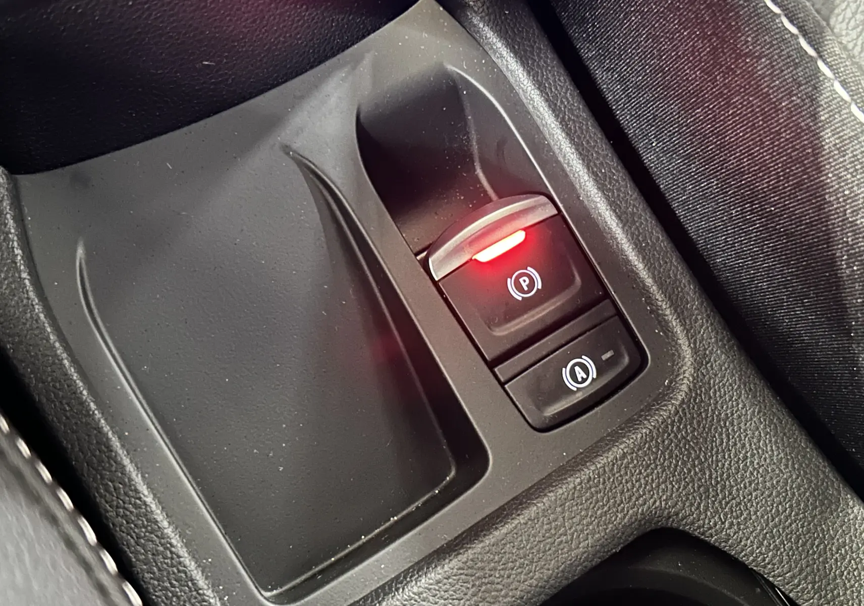 Gros plan sur la console centrale de la Renault Clio V hybride, bouton frein à main électrique avec témoin rouge allumé.