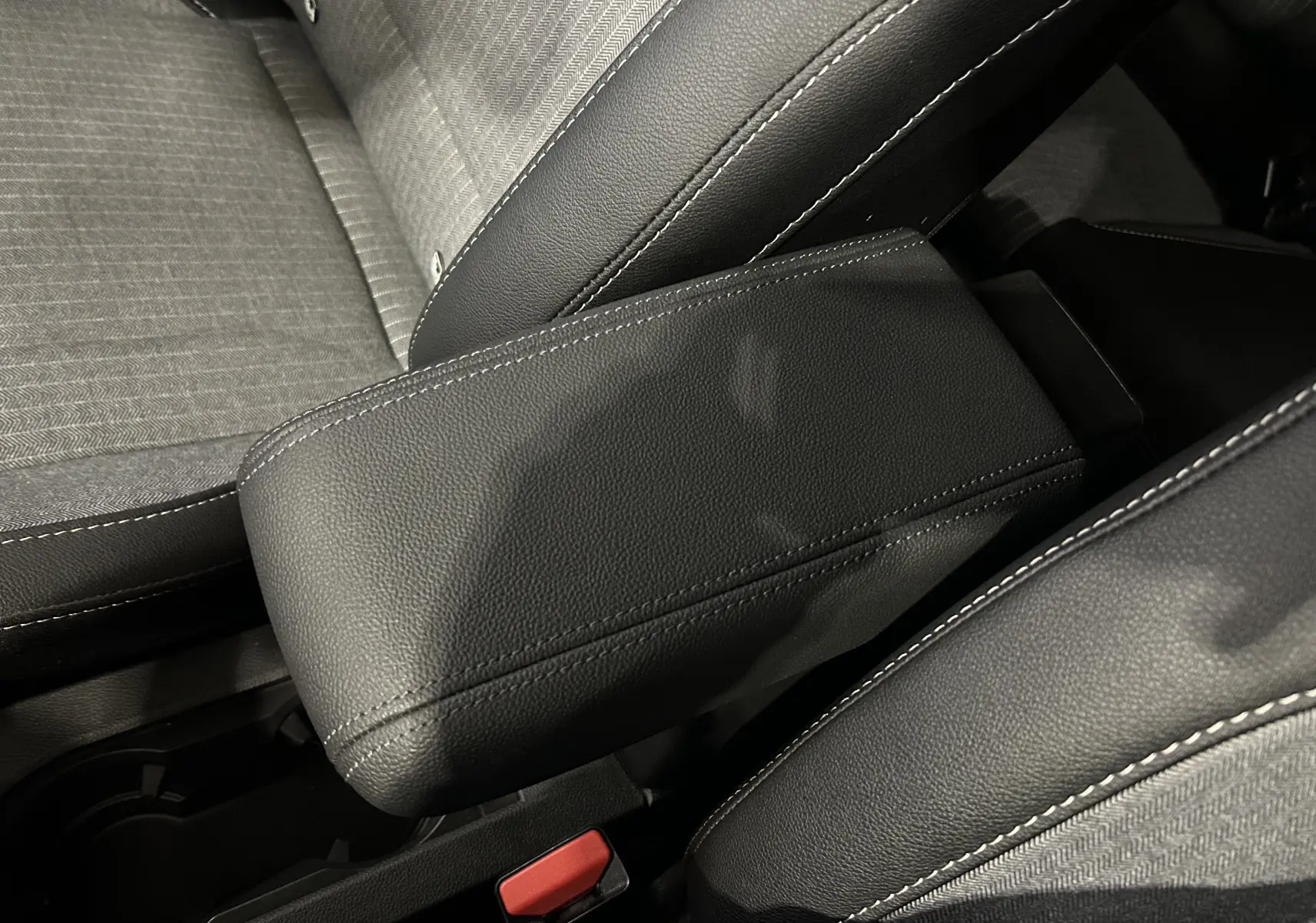 Gros plan sur l'accoudoir central en cuir noir avec surpiqûres blanches, sièges tissu gris et noir Renault Clio V E-Tech.