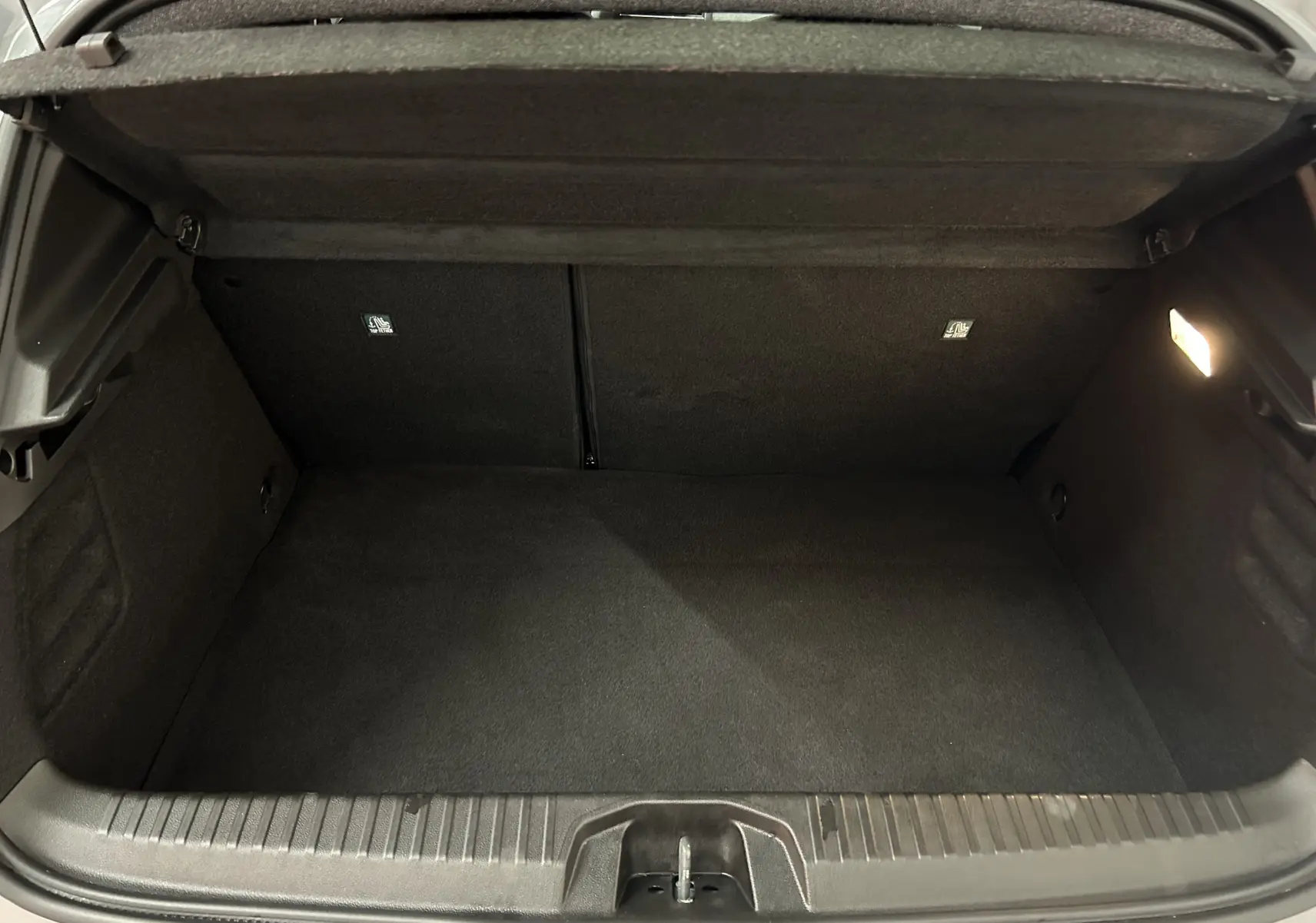Vue intérieure du coffre spacieux et propre de la Renault Clio V E-Tech Full Hybrid 145 Gris Rafale, éclairage latéral allumé.