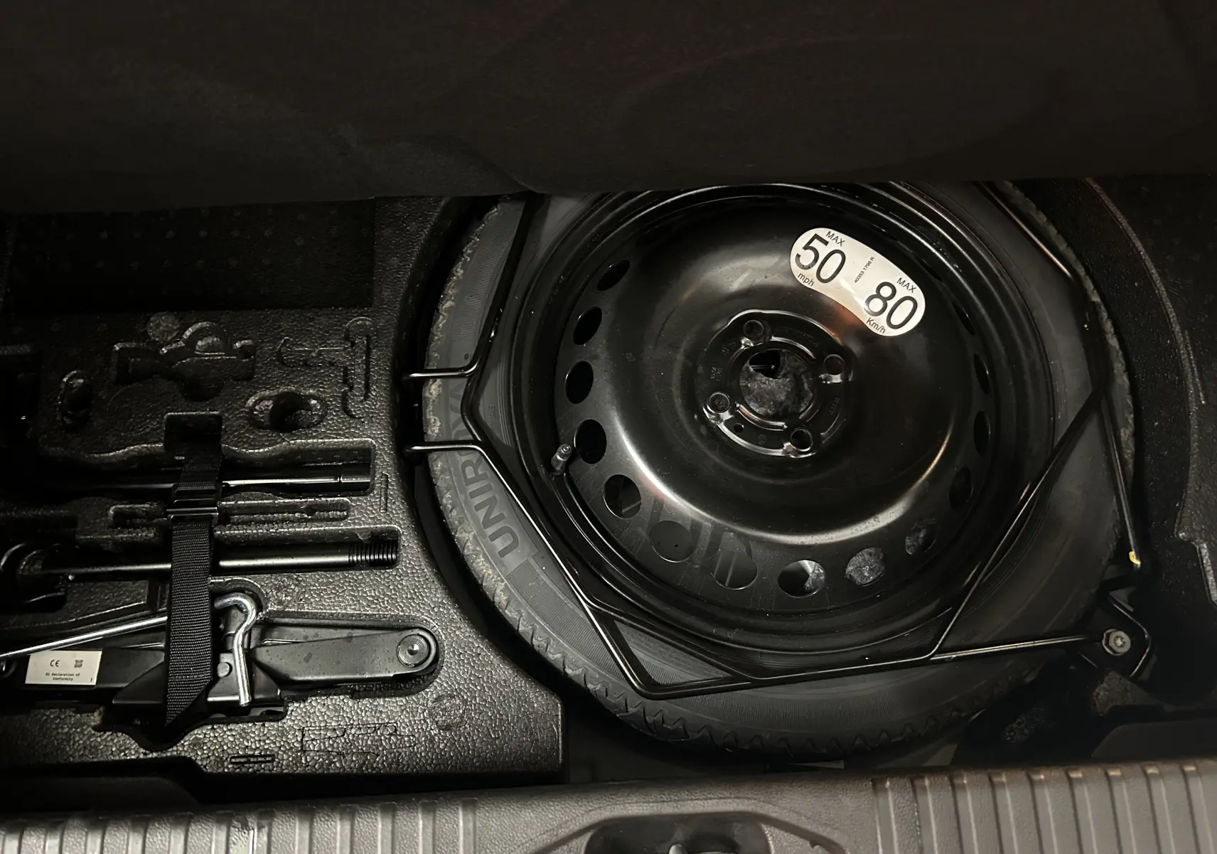 Vue rapprochée de la roue de secours noire et des outils de bord dans le coffre d'une Renault Clio V gris Rafale.