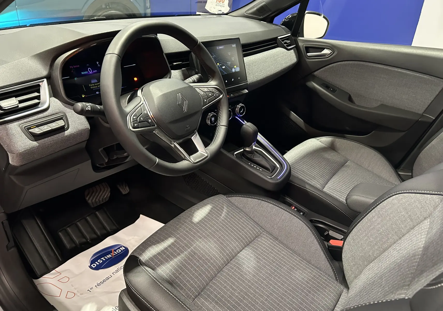 Vue intérieure côté conducteur de la Renault Clio V E-Tech gris rafale, avec tableau de bord digital et sellerie tissu gris.