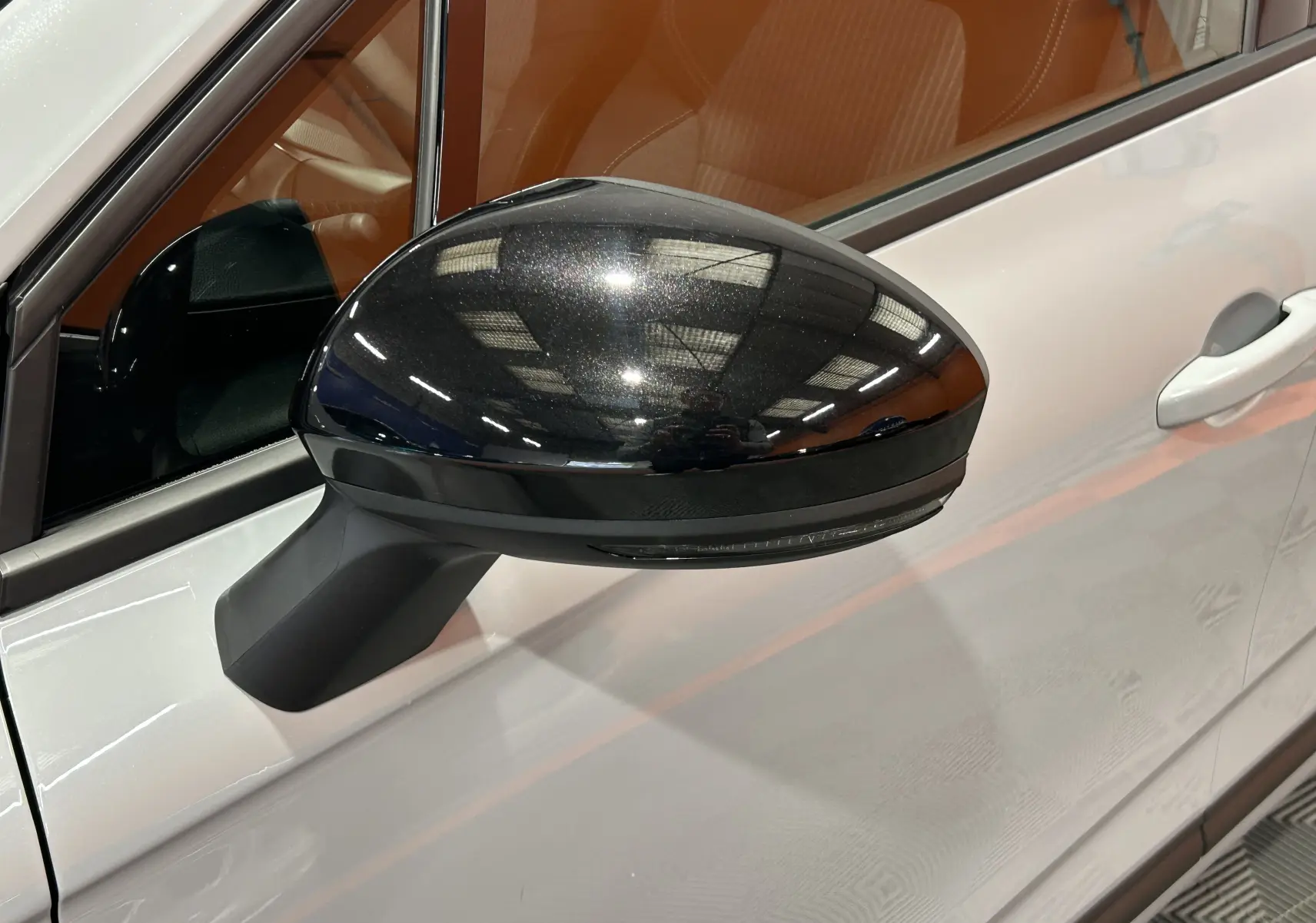Rétroviseur noir brillant côté gauche d'une Renault Clio V gris Rafale, avec porte et poignée visibles.