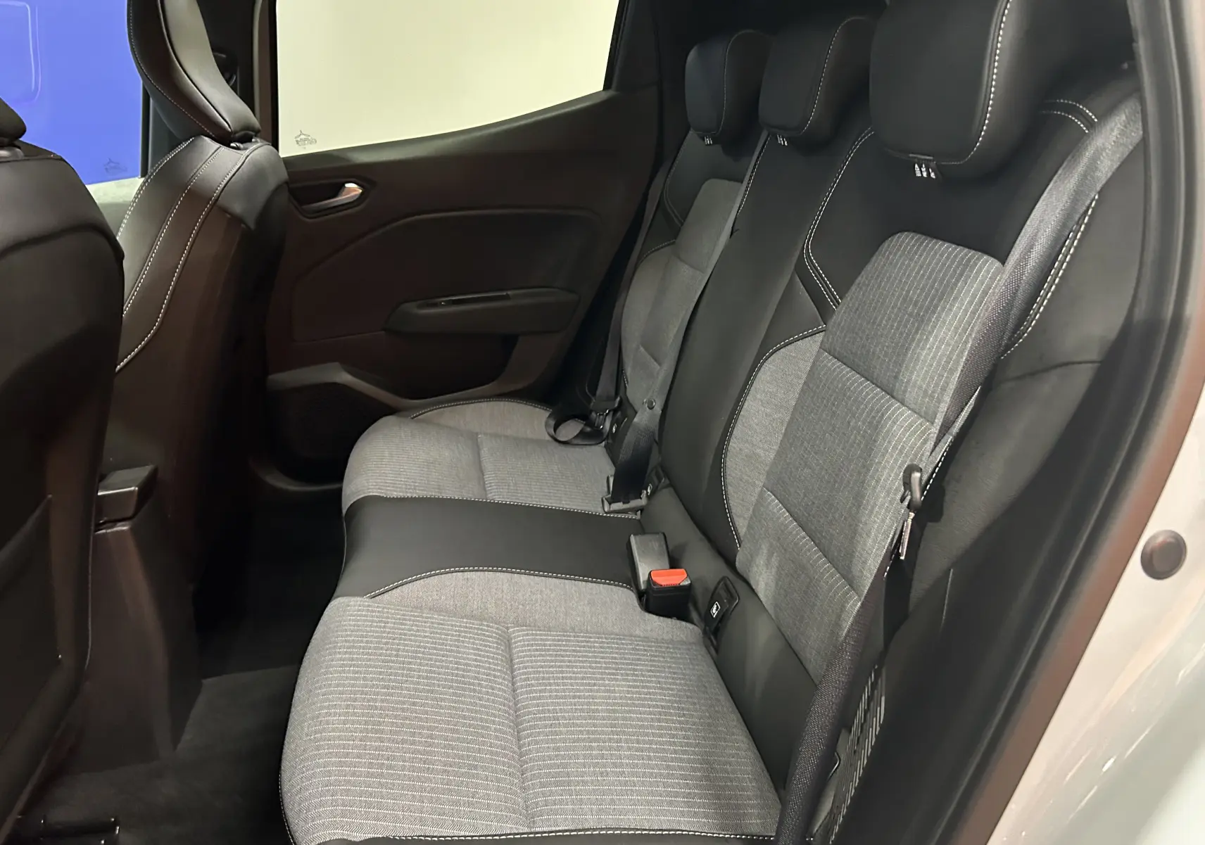Vue latérale droite de l'intérieur arrière de la Renault Clio V gris Rafale, sièges tissu gris et noir avec surpiqûres blanches.