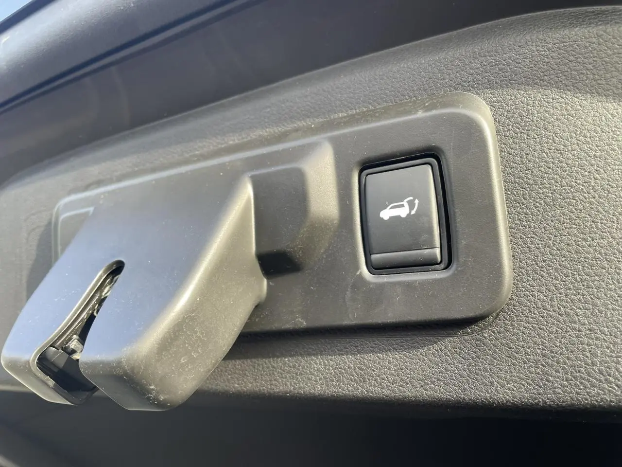 Gros plan sur le bouton d'ouverture du hayon électrique dans un Renault Espace noir étoilé, vue intérieure du coffre.