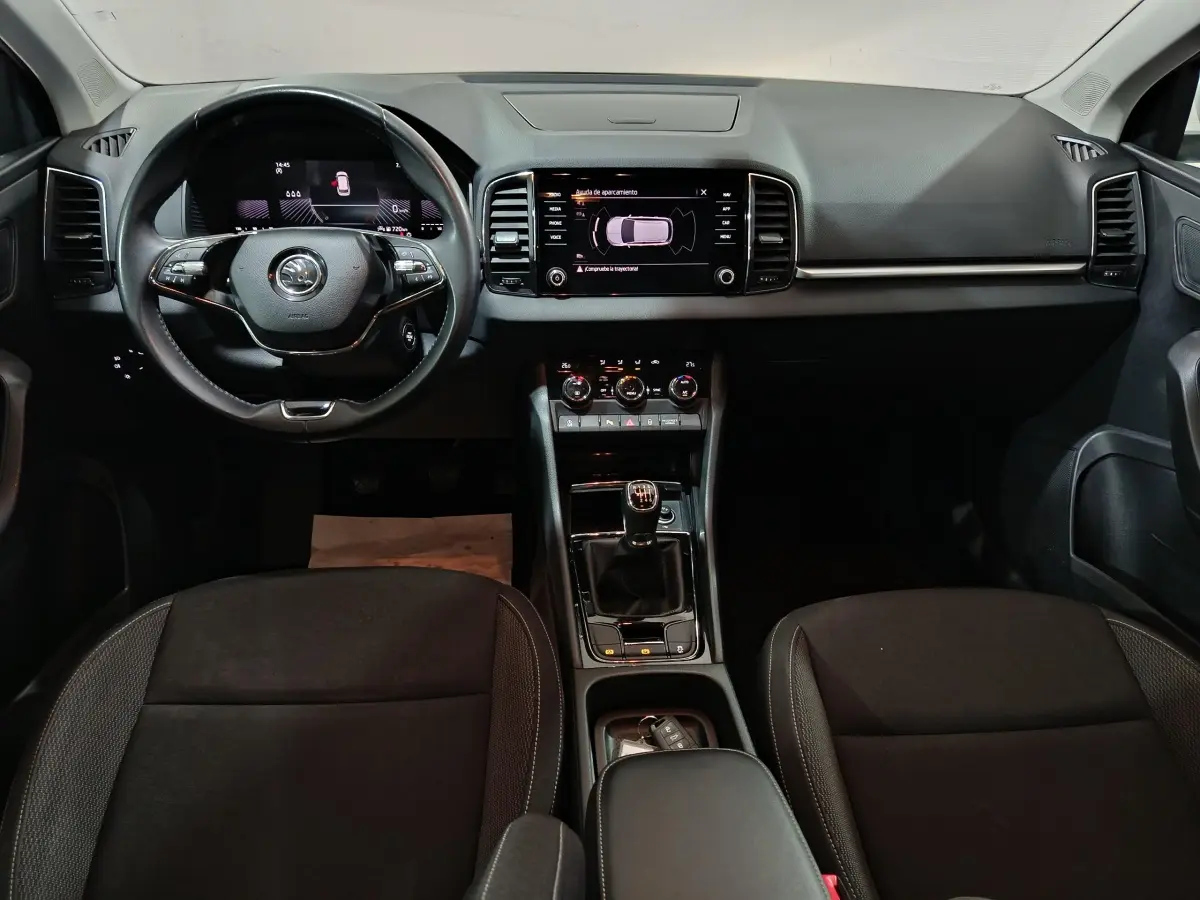 Vue intérieure avant du Skoda Karoq 2.0 TDI 2024, tableau de bord noir avec écran tactile central et volant cuir multifonctions.