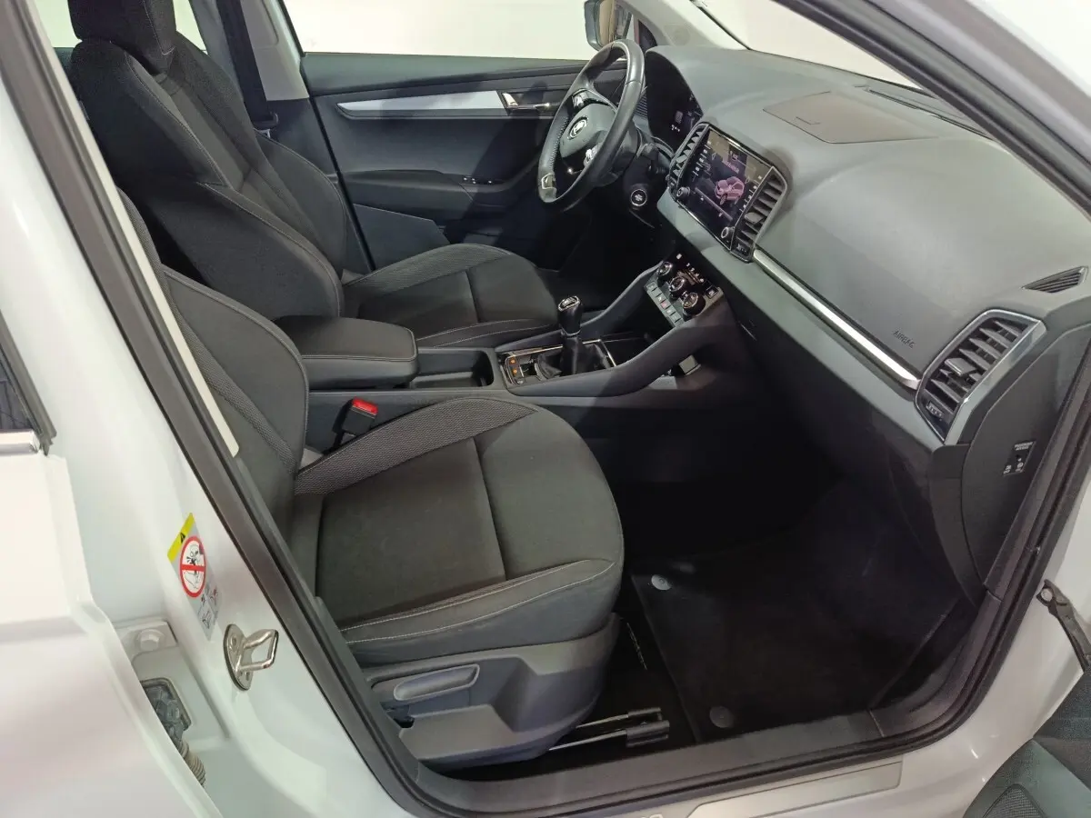 Intérieur côté conducteur d’un Skoda Karoq blanc 2024, avec tableau de bord moderne et sièges noirs en tissu.
