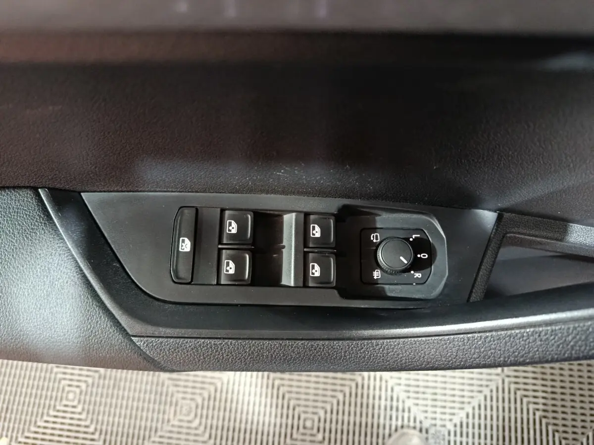 Vue rapprochée des commandes de lève-vitres et réglage des rétroviseurs côté conducteur d’un Skoda Karoq blanc.