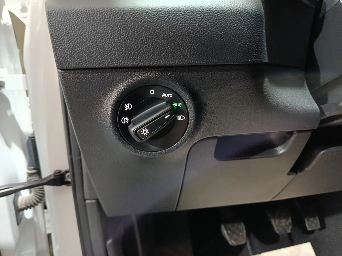 Gros plan sur le bouton de commande des phares noir dans l’habitacle d’un Skoda Karoq blanc, côté conducteur.