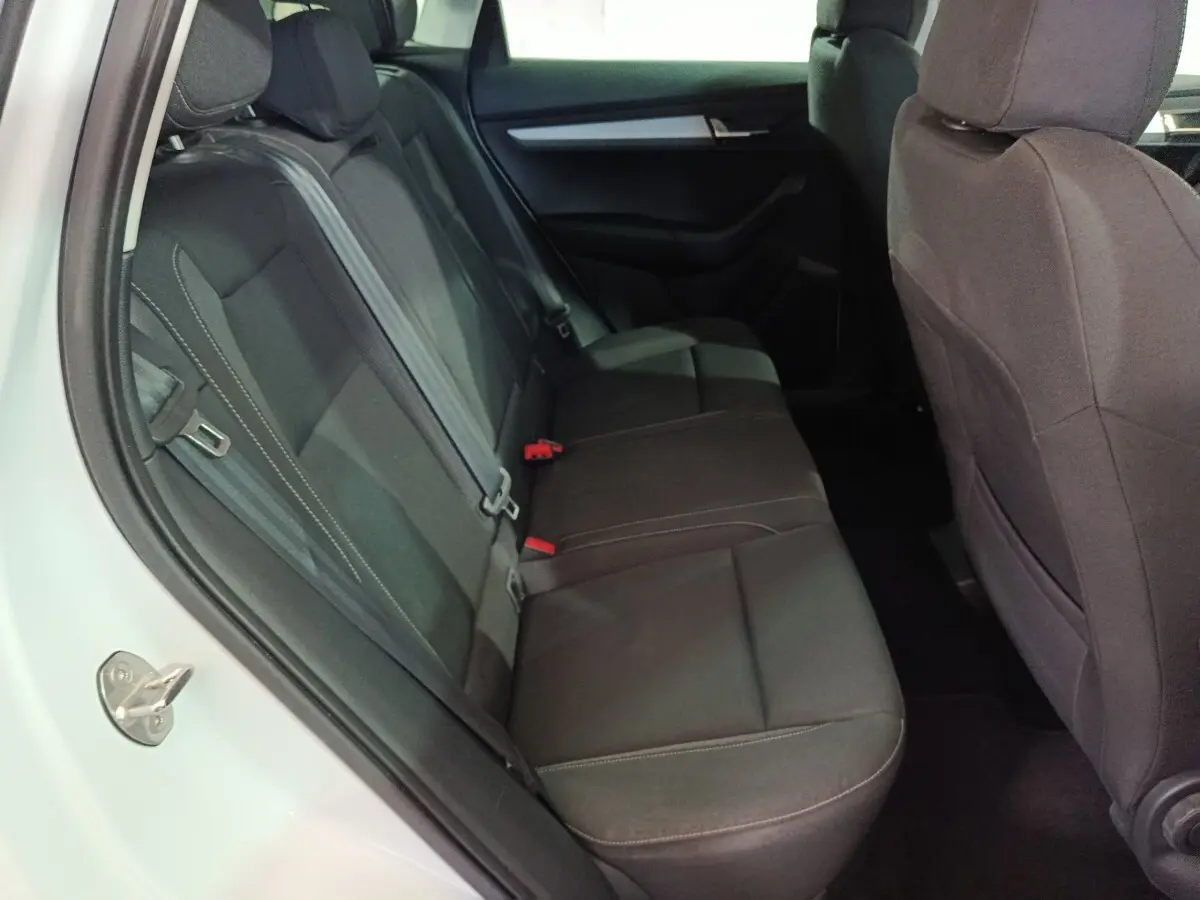 Vue intérieure côté gauche montrant la banquette arrière noire du Skoda Karoq blanc 2024 avec ceintures de sécurité visibles.