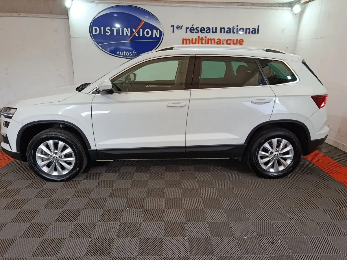 Vue de profil côté gauche d'un Skoda Karoq blanc 2024 avec jantes alliage et barres de toit noires.