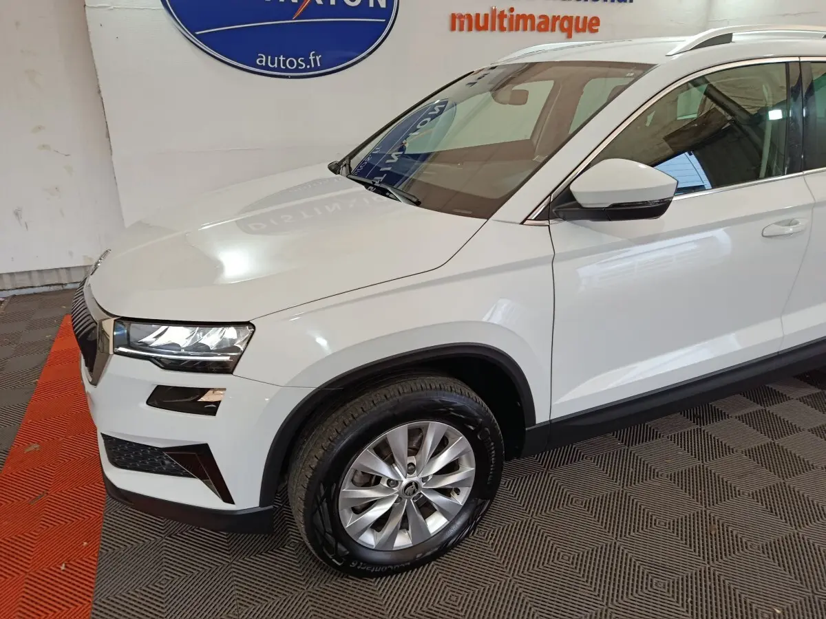 Vue 3/4 avant gauche d'un SKODA KAROQ blanc 2024 avec phares LED et jantes alliage argentées.