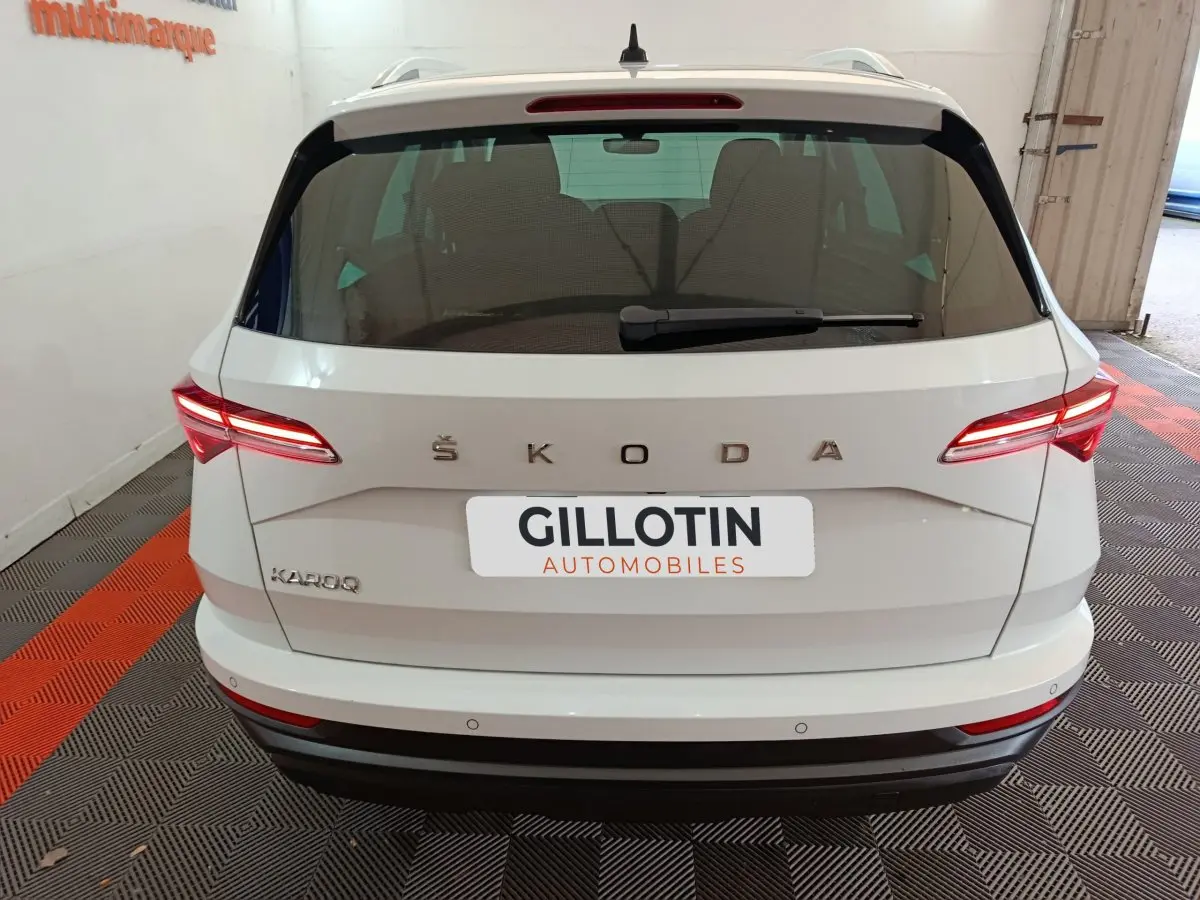 Vue arrière d'un Skoda Karoq blanc 2024 avec feux LED allumés et logo ŠKODA visible sur le hayon.