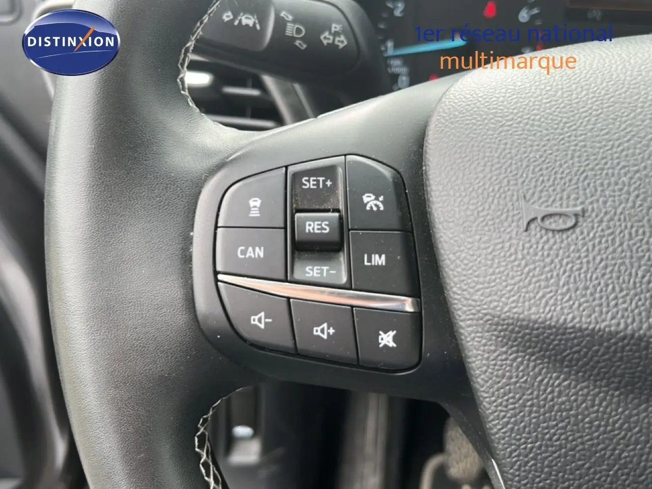 Gros plan sur les commandes du volant noir du Ford Puma gris, montrant les boutons de régulateur et volume sonore.