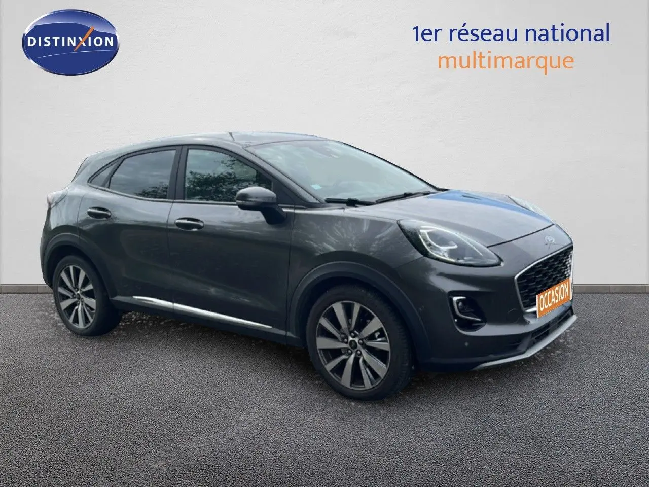 Ford Puma gris en 3/4 avant droit, avec jantes alliage et calandre distinctive, sur fond neutre.