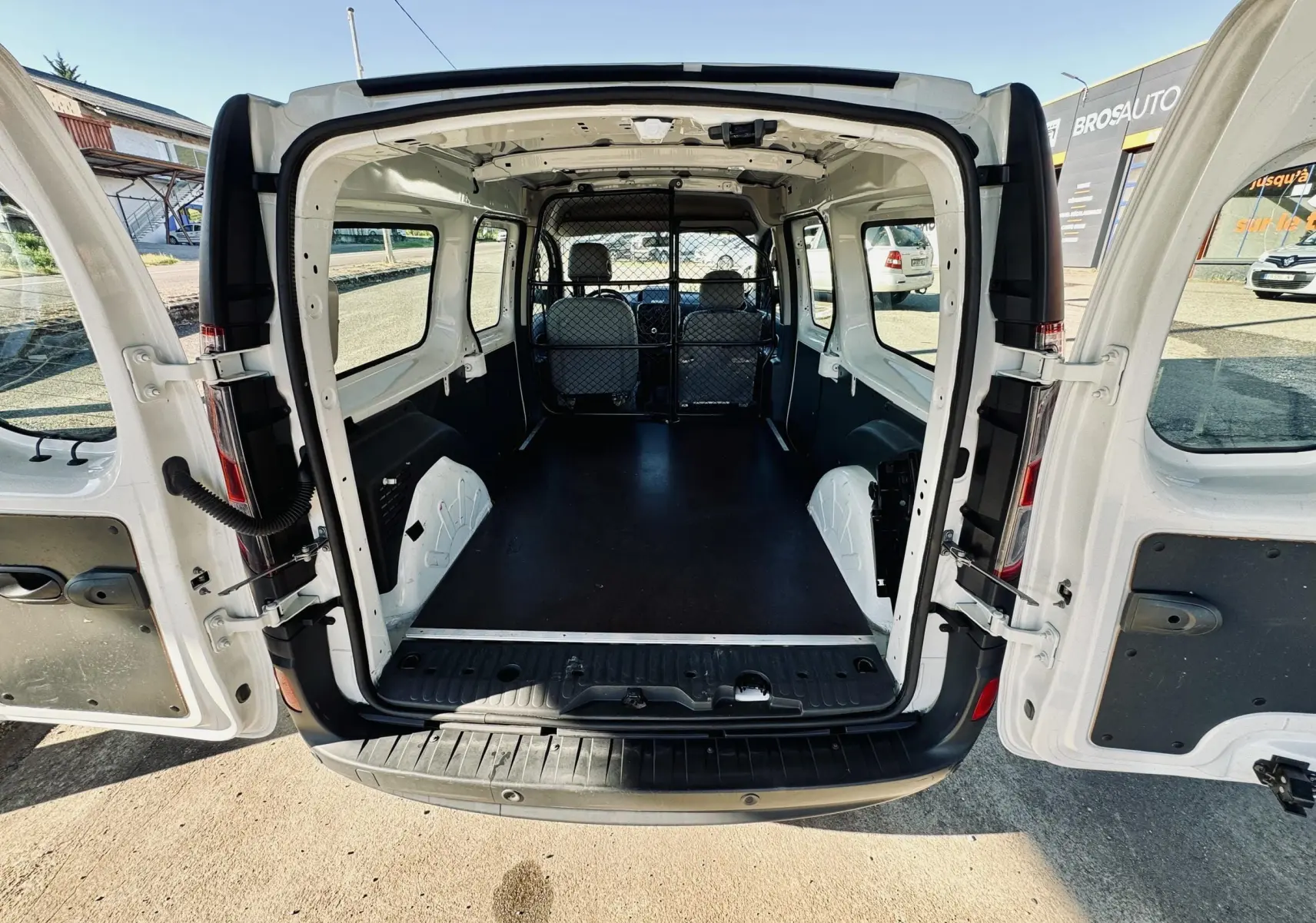 Vue arrière du Renault Kangoo Maxi blanc avec portes ouvertes montrant l’espace de chargement vide et la cloison métallique.