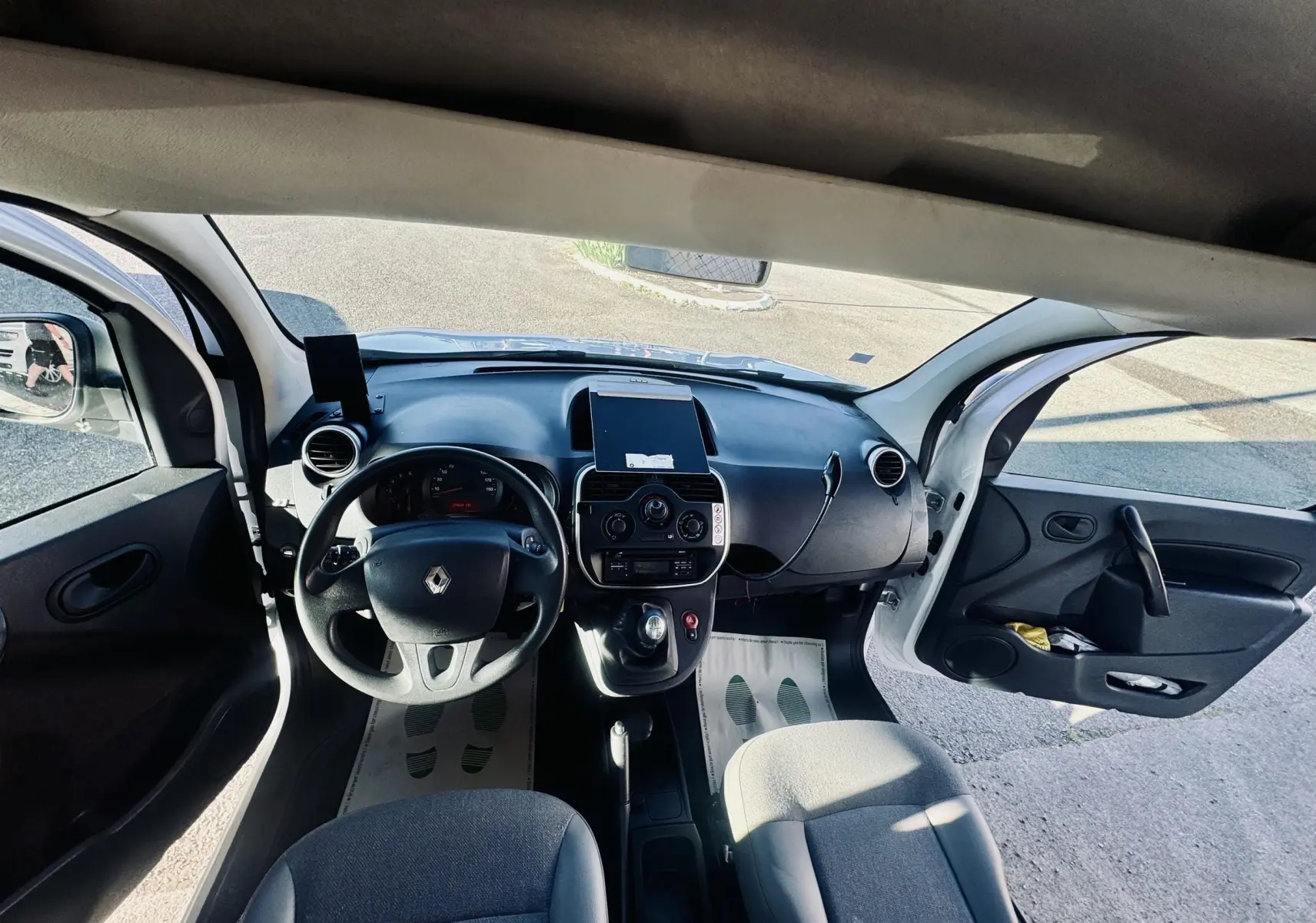 Vue intérieure avant du Renault Kangoo blanc 2021, avec portes ouvertes et tableau de bord noir.