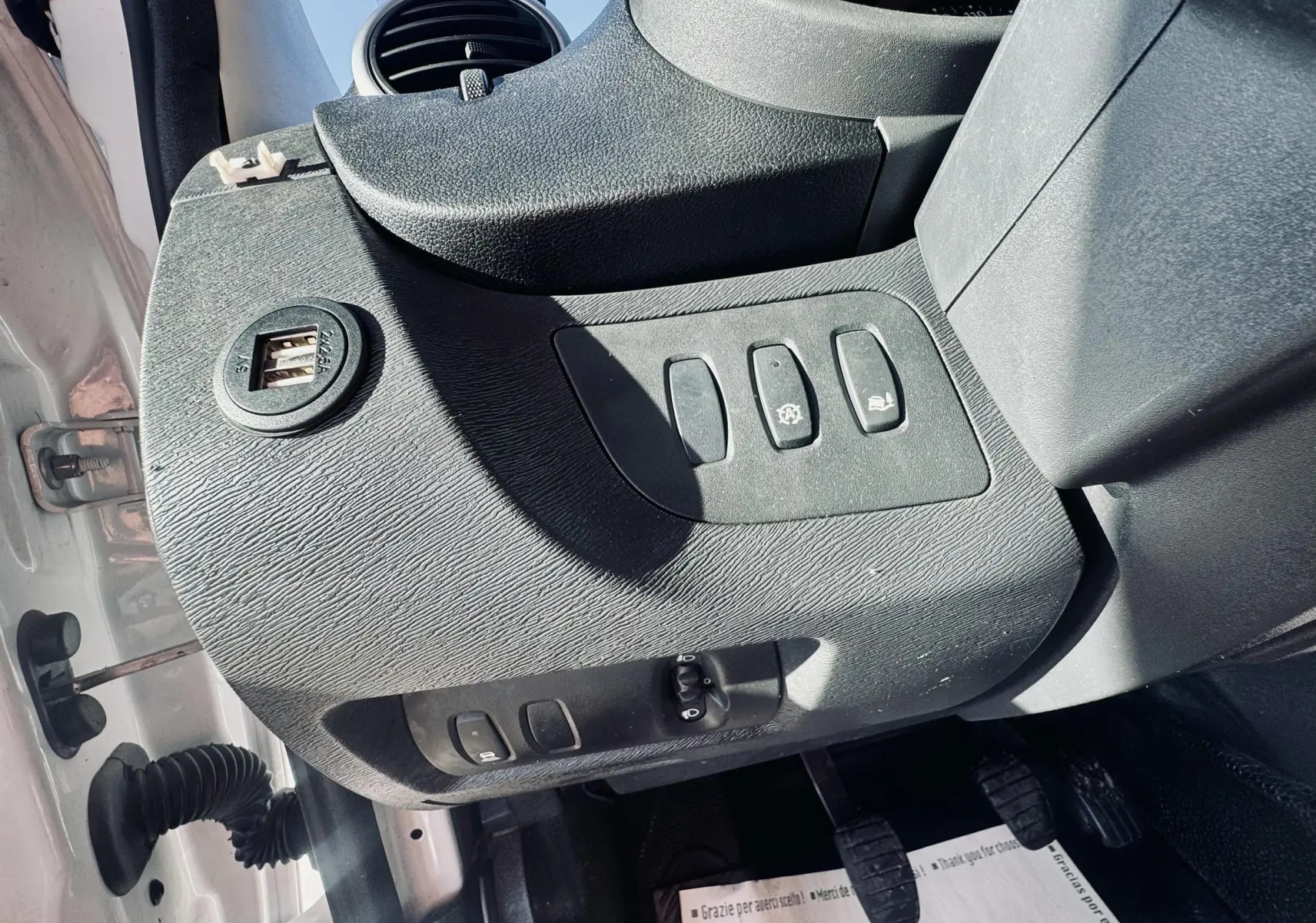 Vue rapprochée de la console côté gauche du Renault Kangoo blanc, montrant les boutons de commande et une prise USB double.