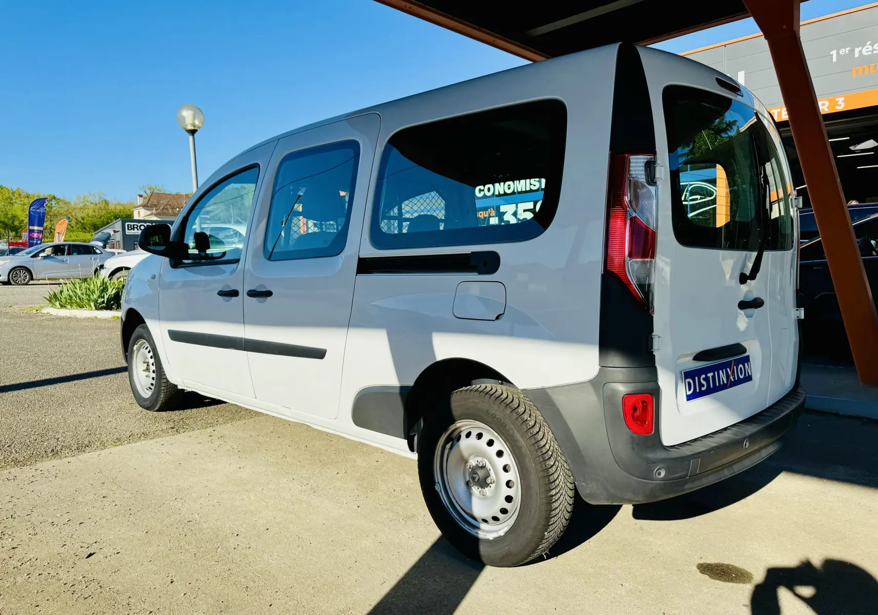 Vue 3/4 arrière droite d’un Renault Kangoo Maxi blanc avec vitres teintées et pare-chocs noirs, stationné en extérieur.