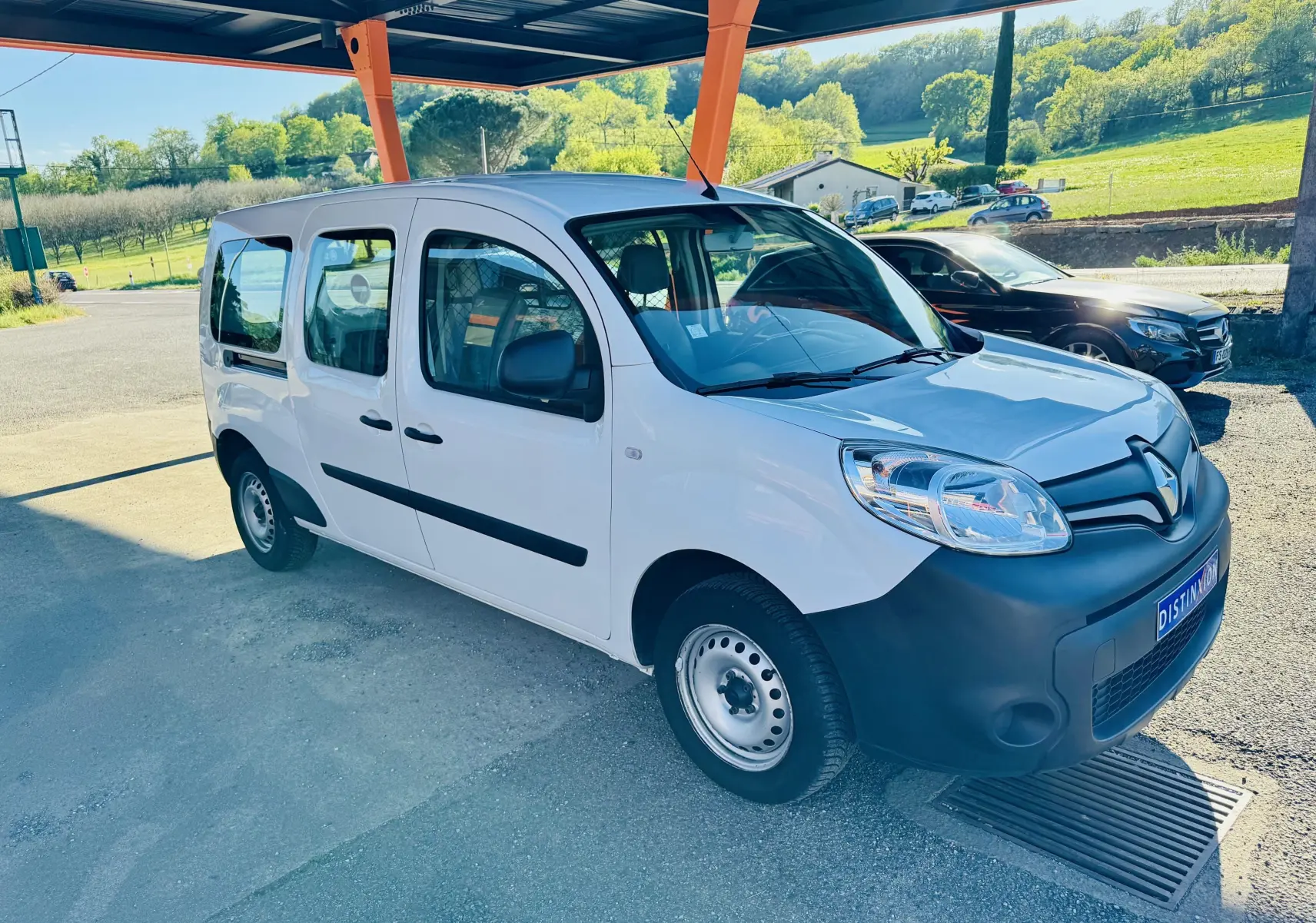 Renault Kangoo Maxi blanc en 3/4 avant droit sous abri, avec pare-chocs noir et jantes acier simples.