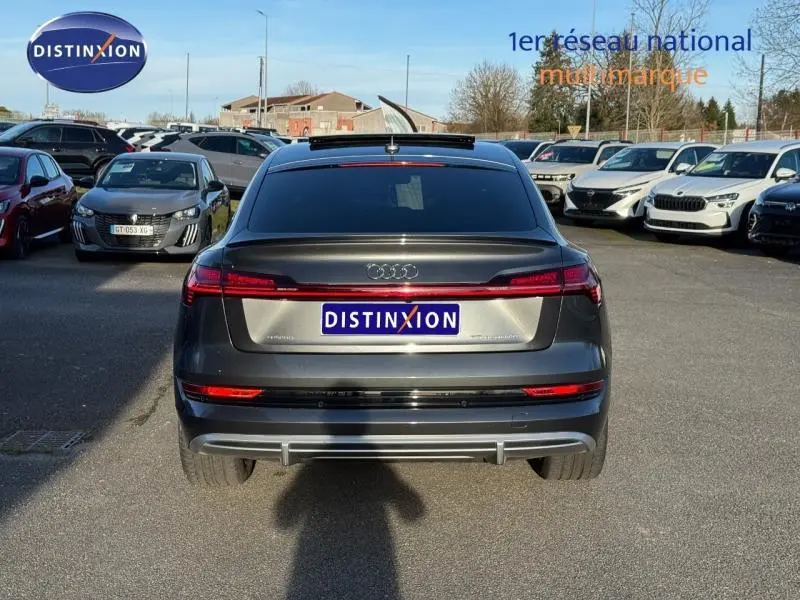 Vue arrière d'une Audi E-Tron Sportback gris foncé métal, avec feux LED et lunette arrière teintée, stationnée en extérieur.