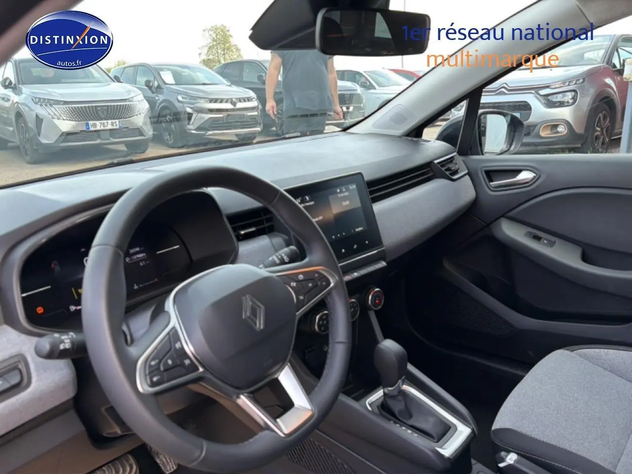 Vue intérieure côté conducteur de la Renault Clio V gris, volant multifonction et tableau de bord moderne avec écran tactile.