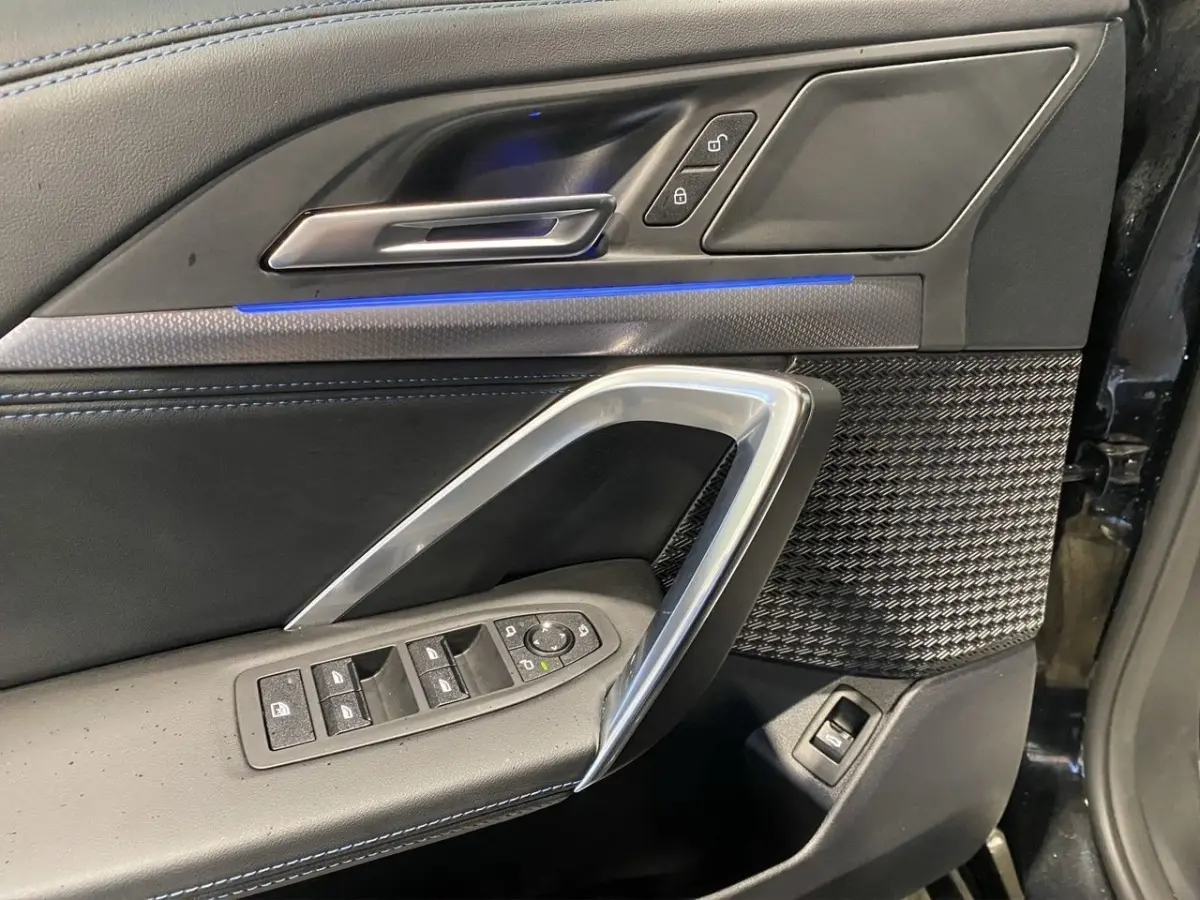 Vue rapprochée de la porte avant gauche noire du BMW X1 2025 avec éclairage d'ambiance bleu et commandes électriques.
