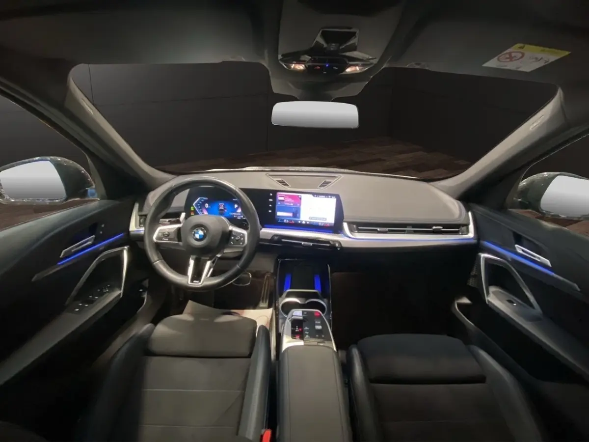 Intérieur noir du BMW X1 2025 vu de face, tableau de bord moderne avec écran tactile et éclairage d'ambiance bleu.