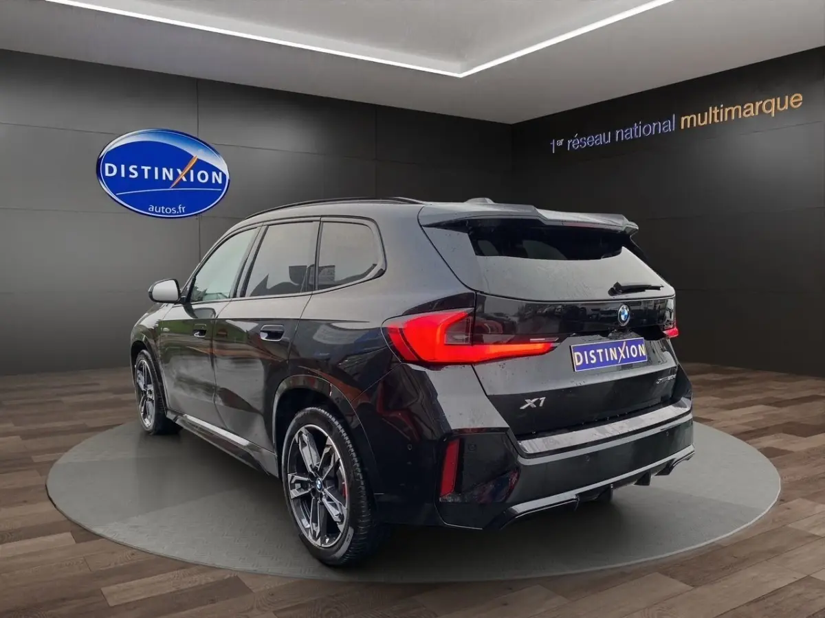BMW X1 noir en 3/4 arrière droit, avec feux LED distinctifs et jantes sport M visibles en showroom.