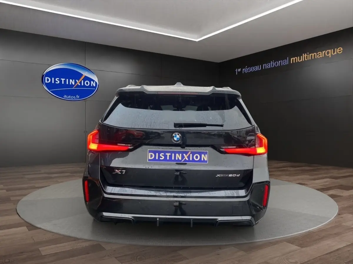 Vue arrière d'un BMW X1 noir xDrive20d avec feux LED caractéristiques et logo distinctif sur fond showroom.