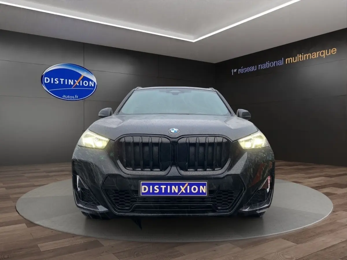 Vue frontale d’un BMW X1 noir avec calandre noire et phares allumés dans un showroom.