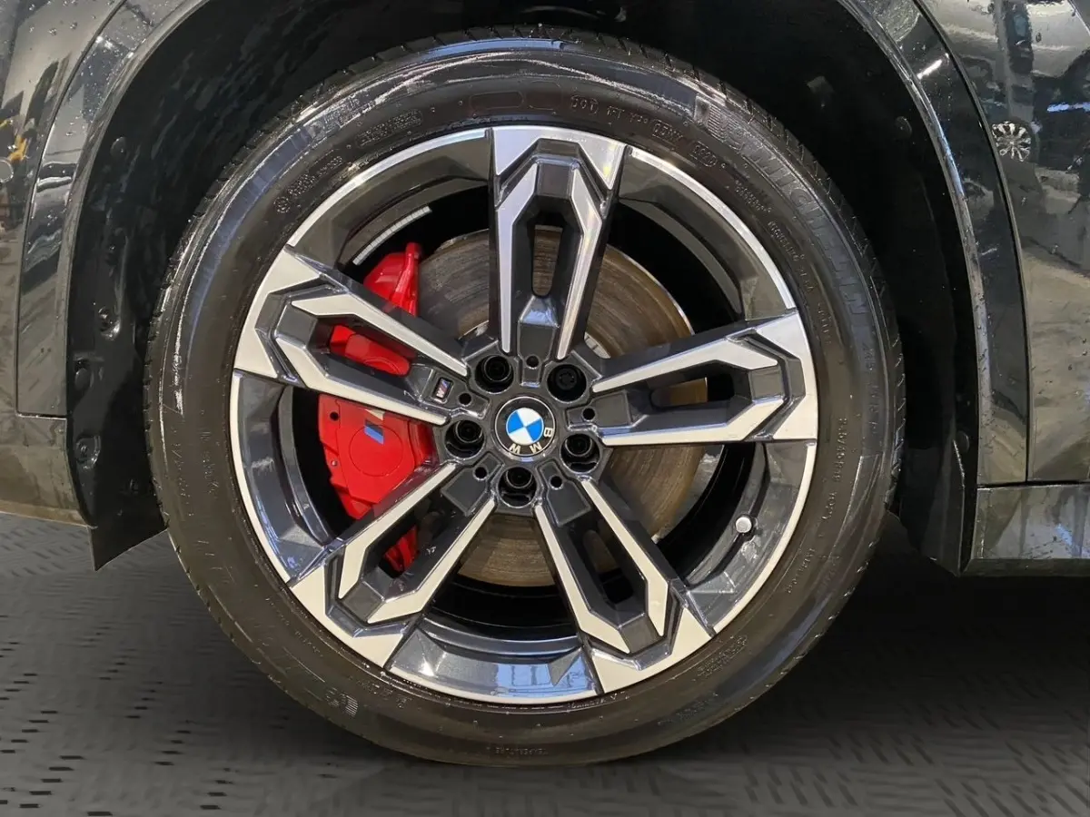 Gros plan sur la roue avant gauche noire d'une BMW X1 2025 avec étrier de frein rouge et jante alu bicolore M Sport.