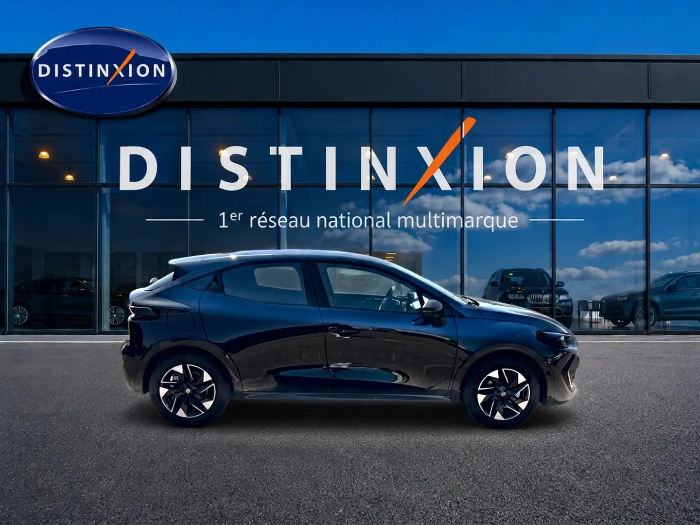 Profil latéral droit d'une Renault Clio VI noire 2026, avec jantes alliage et vitres teintées, devant une vitrine Distinxion.