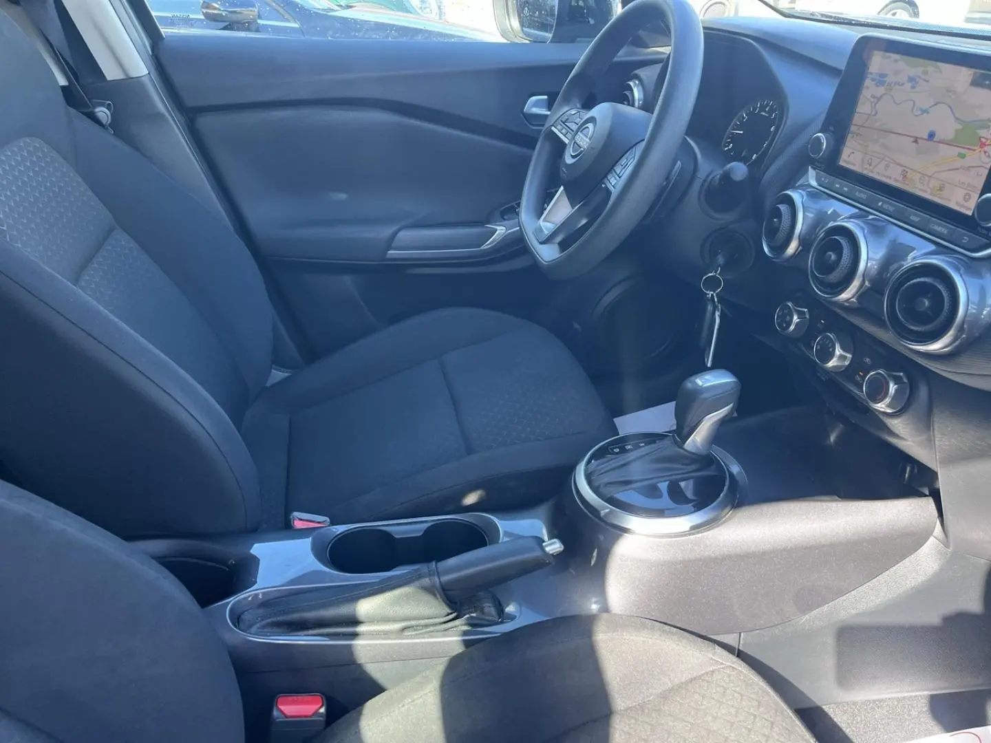 Intérieur avant du Nissan Juke 2023 vu côté conducteur, sièges tissu noir et écran tactile GPS visible.