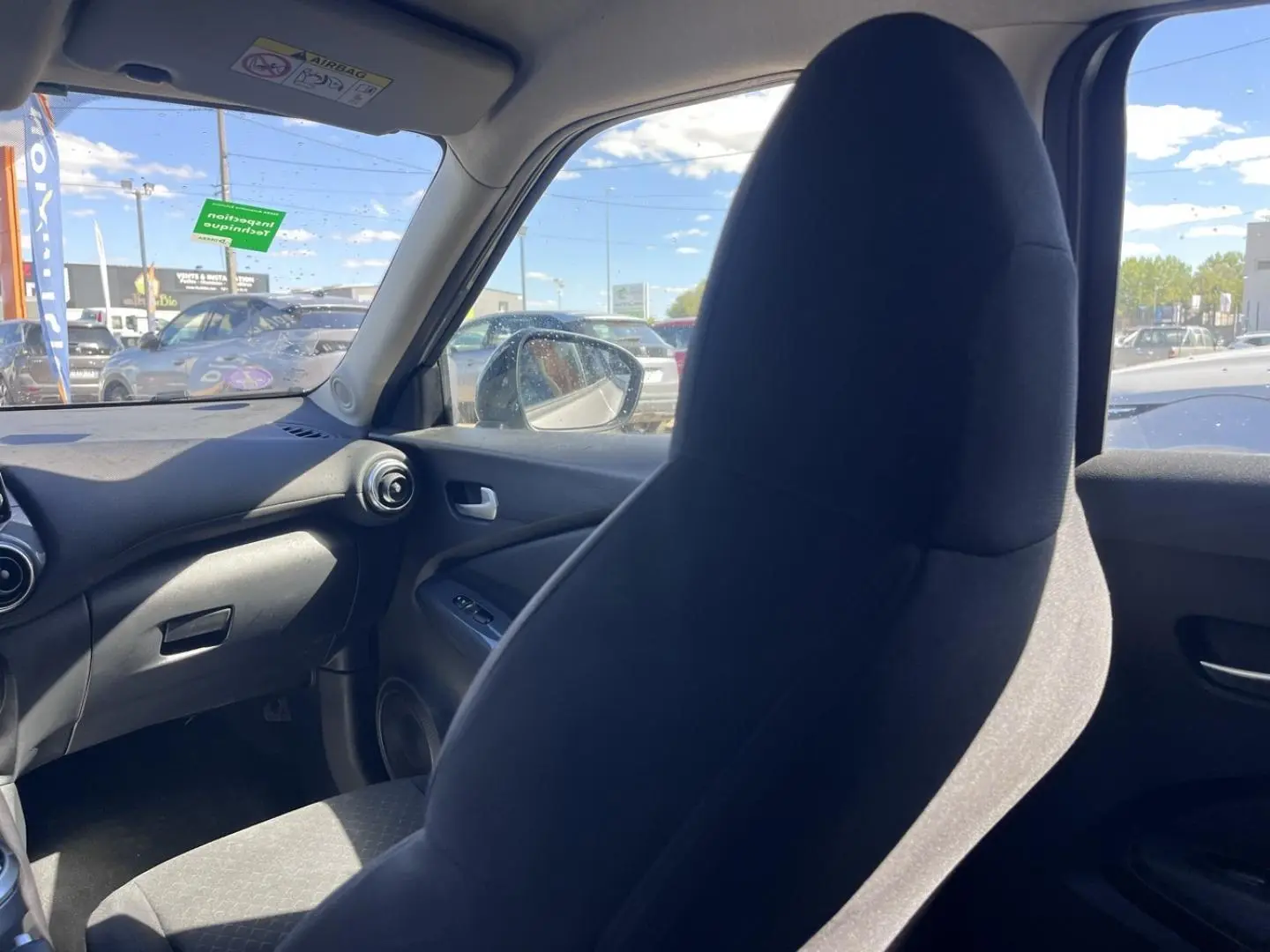 Intérieur de Nissan Juke 2023 vu côté passager, siège tissu noir et tableau de bord gris foncé.