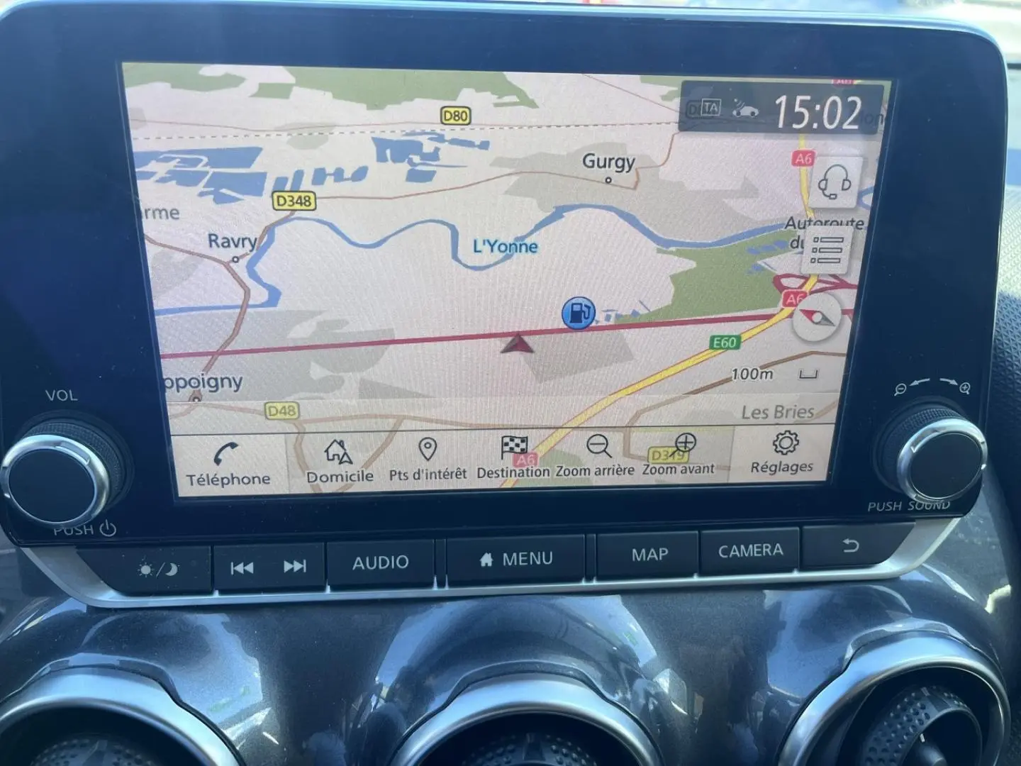 Écran tactile central du Nissan Juke 2023 affichant la navigation GPS avec commandes audio et caméra en dessous.