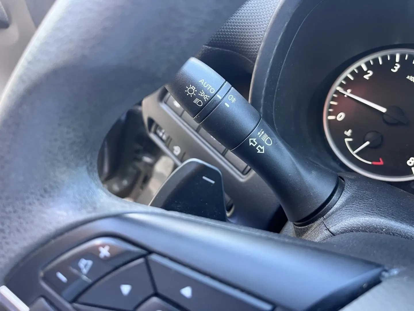 Gros plan sur la commande de clignotants et palettes au volant noir du Nissan Juke gris Argile 2023.
