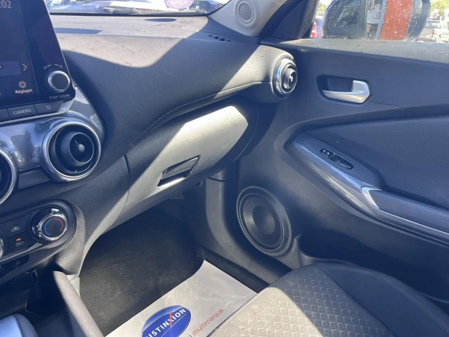 Vue intérieure côté passager du tableau de bord et porte d’une Nissan Juke 2023 avec sellerie tissu noir et finitions argentées.