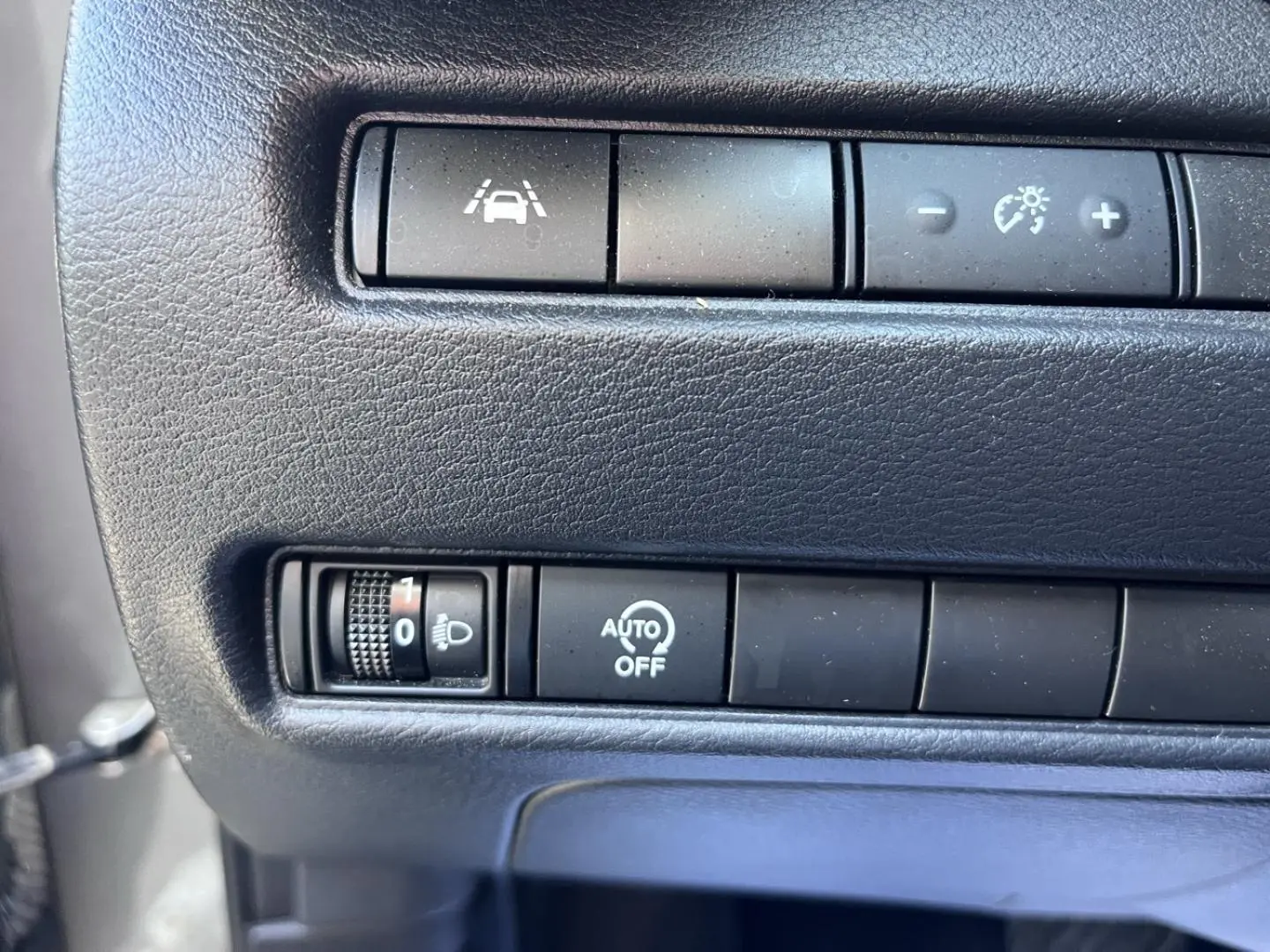 Gros plan sur les commandes de réglage des phares et d'aide à la conduite dans un Nissan Juke gris argile 2023.