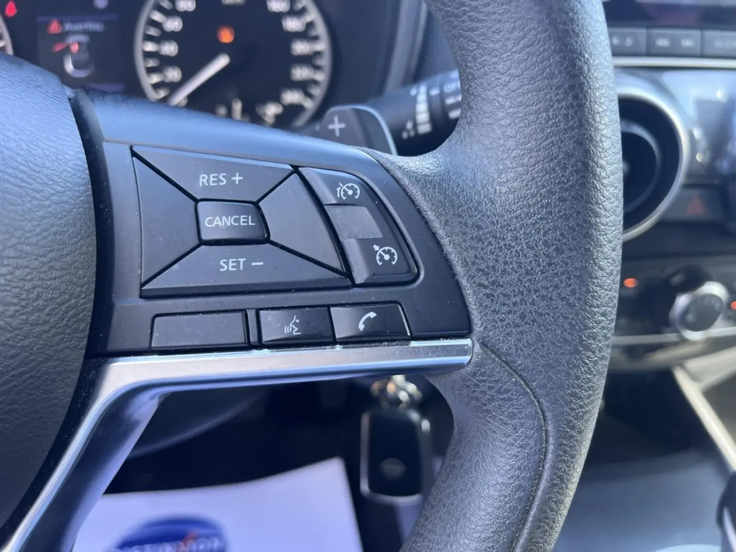 Gros plan sur les commandes au volant noir du Nissan Juke 2023, avec tableau de bord et écran tactile en arrière-plan.