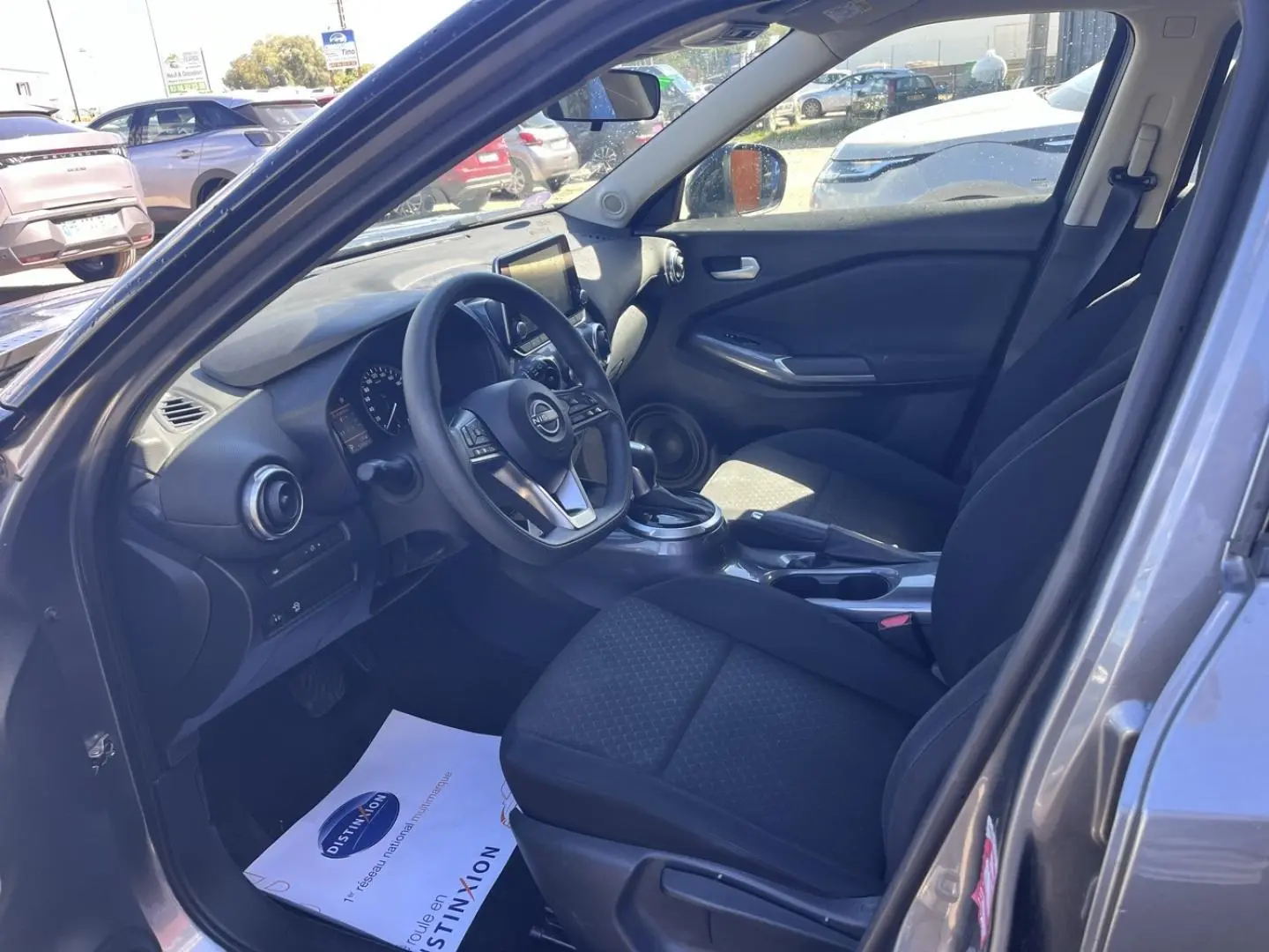 Intérieur avant droit du Nissan Juke 2023 gris Argile, sièges tissu noir et tableau de bord avec écran tactile.