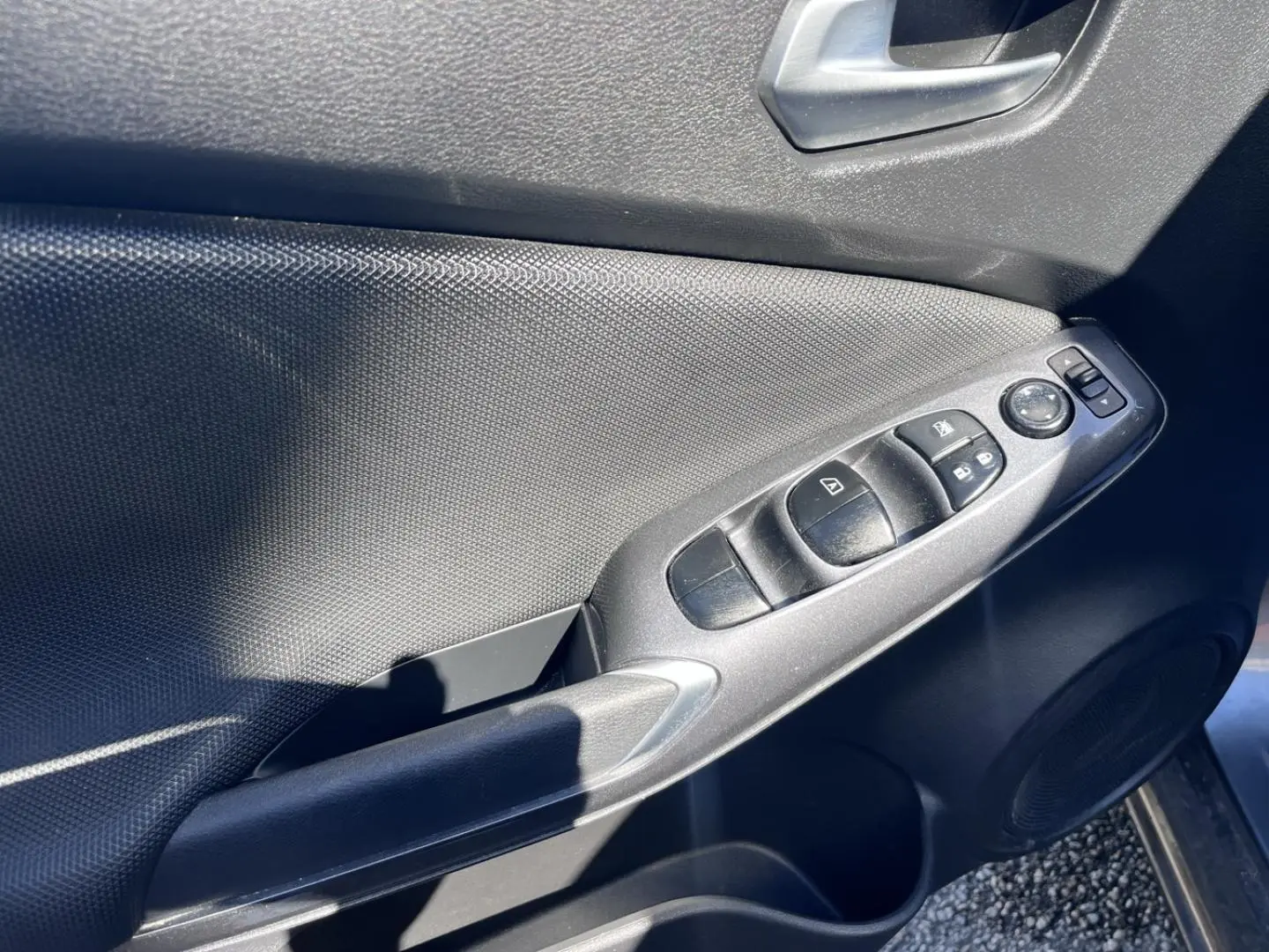 Panneau de porte côté conducteur du Nissan Juke 2023 gris, avec commandes électriques des vitres et rétroviseurs.