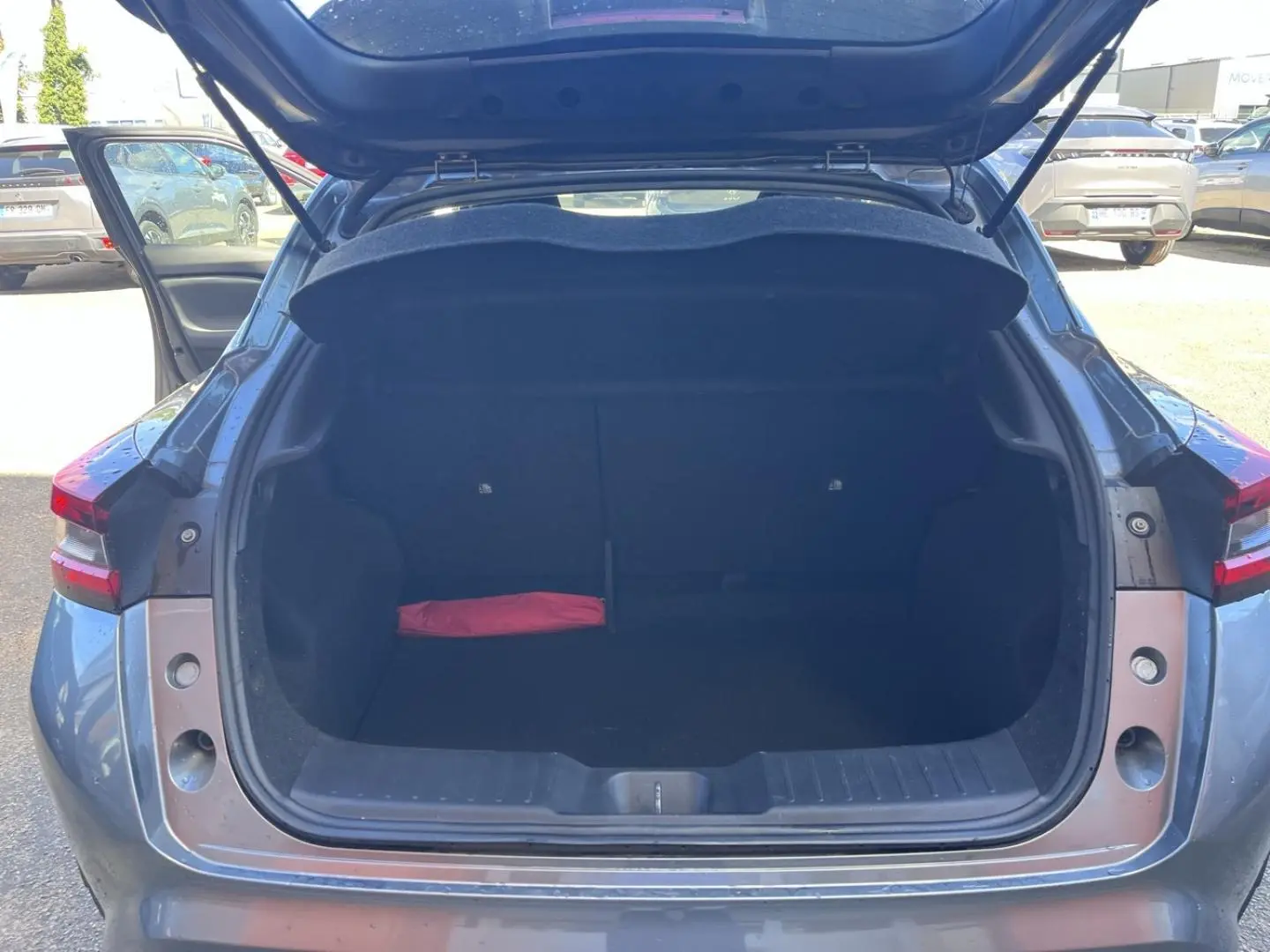 Coffre ouvert vu de l'arrière d'un Nissan Juke 2023 gris Argile Spéciale avec un objet rouge à l'intérieur.