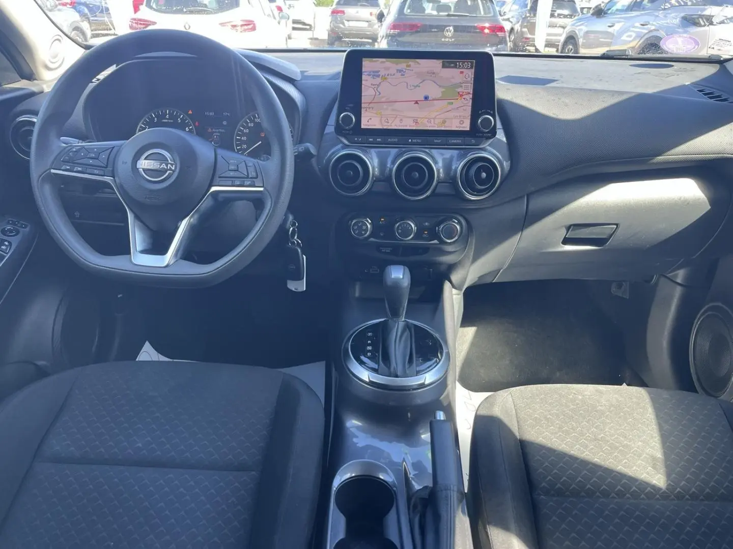 Vue intérieure avant du Nissan Juke 2023 avec tableau de bord noir, écran tactile GPS et volant multifonction.