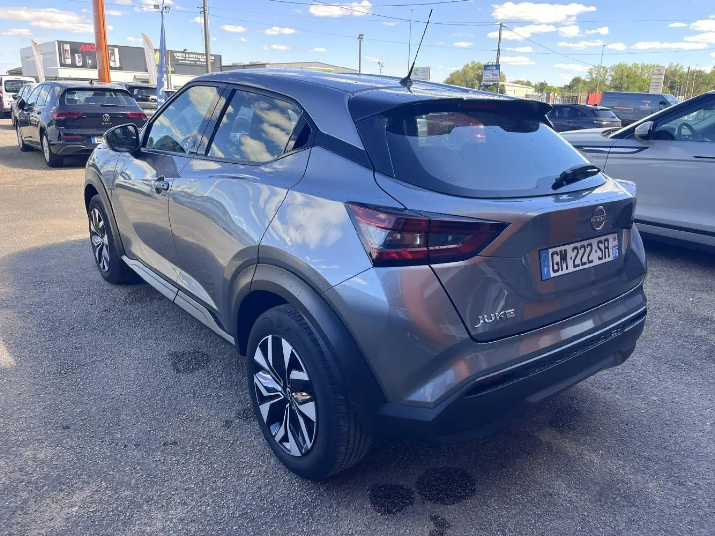 Nissan Juke 2023 gris argile vue 3/4 arrière droit avec jantes bi-ton et toit noir brillant.
