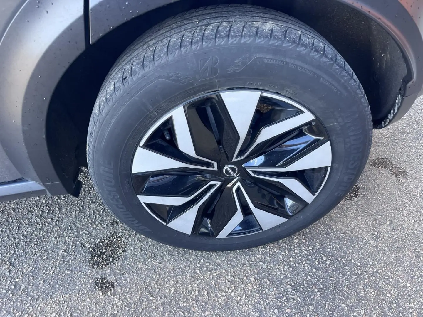 Gros plan sur la roue avant droite d’une Nissan Juke 2023 gris argile avec jante alliage bicolore.