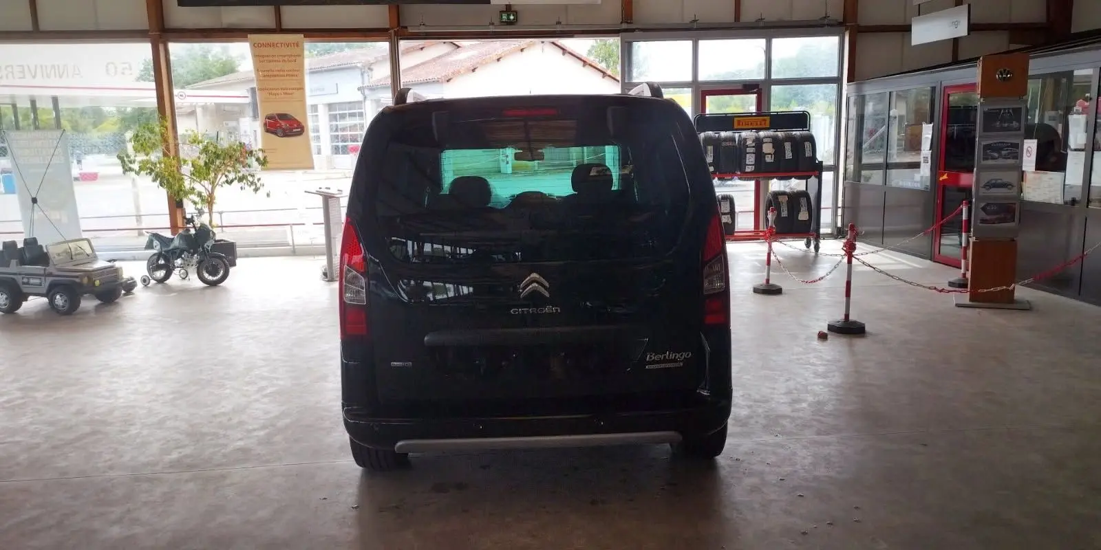 Vue arrière d'un Citroën Berlingo noir 2016 exposé en intérieur, avec vitres teintées et feux verticaux rouges.