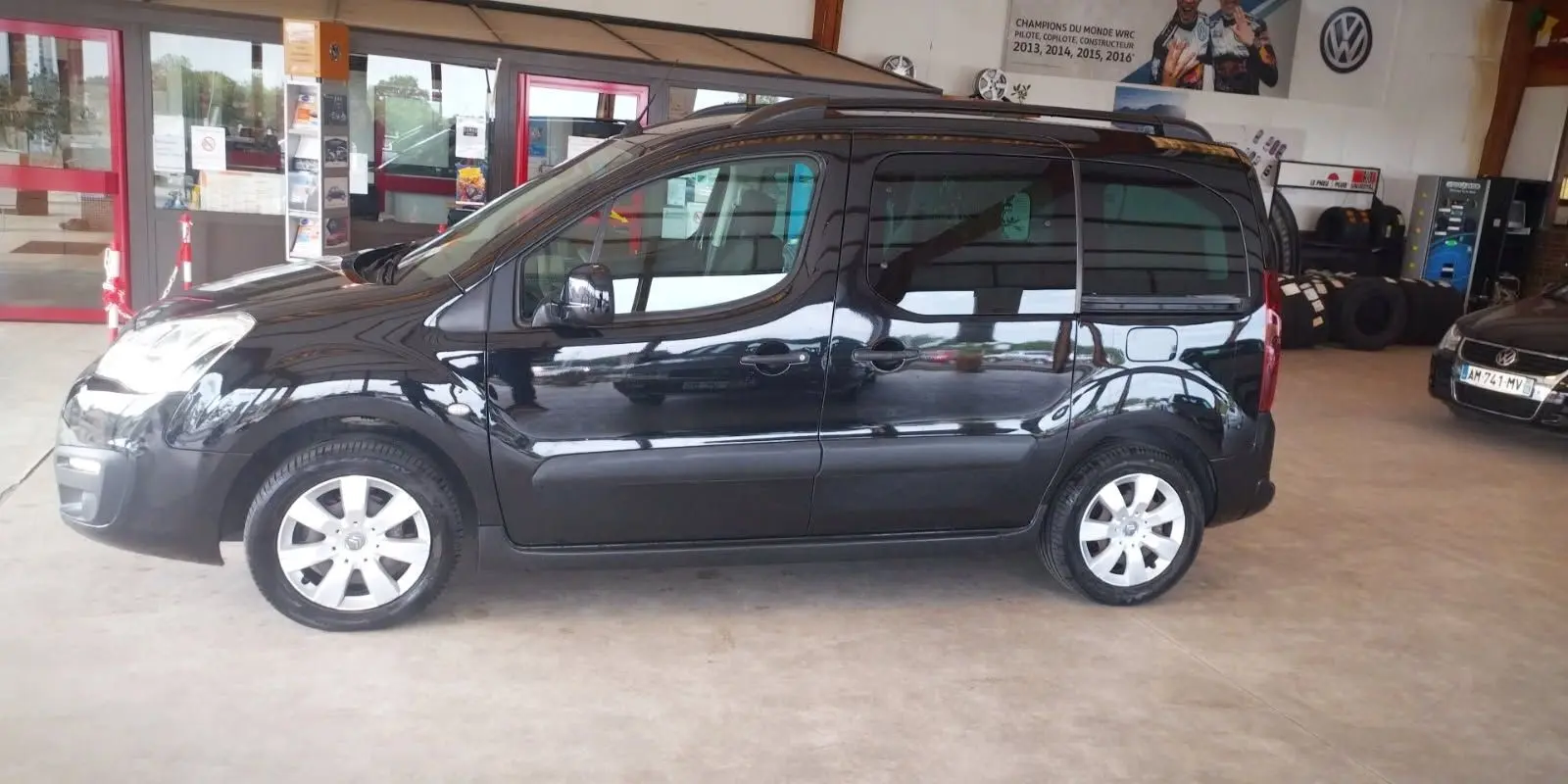 Profil côté gauche d'un Citroën Berlingo noir 2016 en intérieur, soulignant ses lignes compactes et ses jantes argentées.