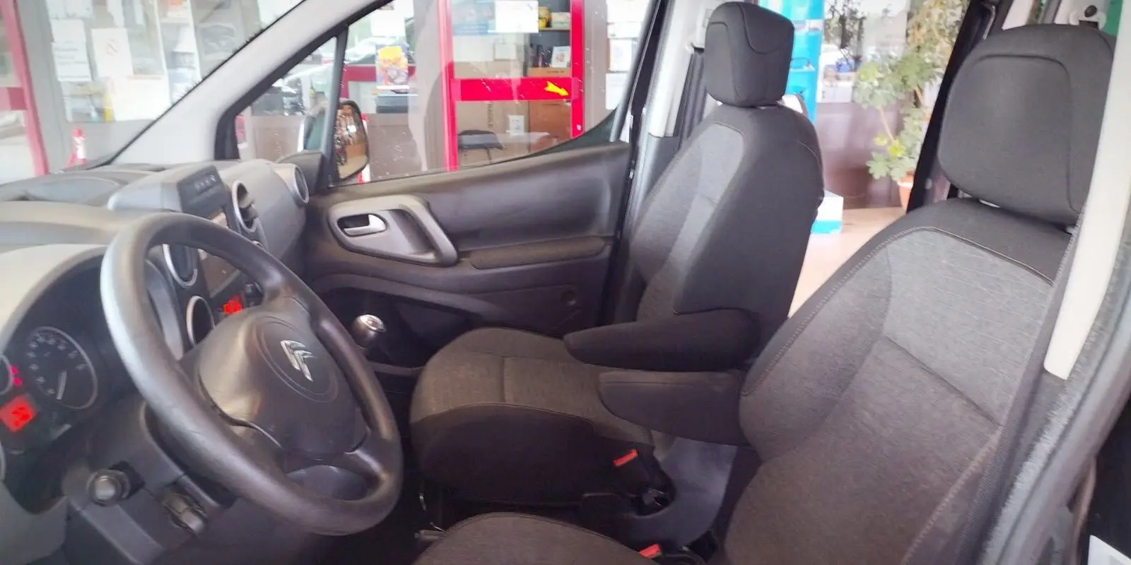 Intérieur avant du Citroën Berlingo 2016 noir, vue côté conducteur avec sièges en tissu gris et volant multifonction.